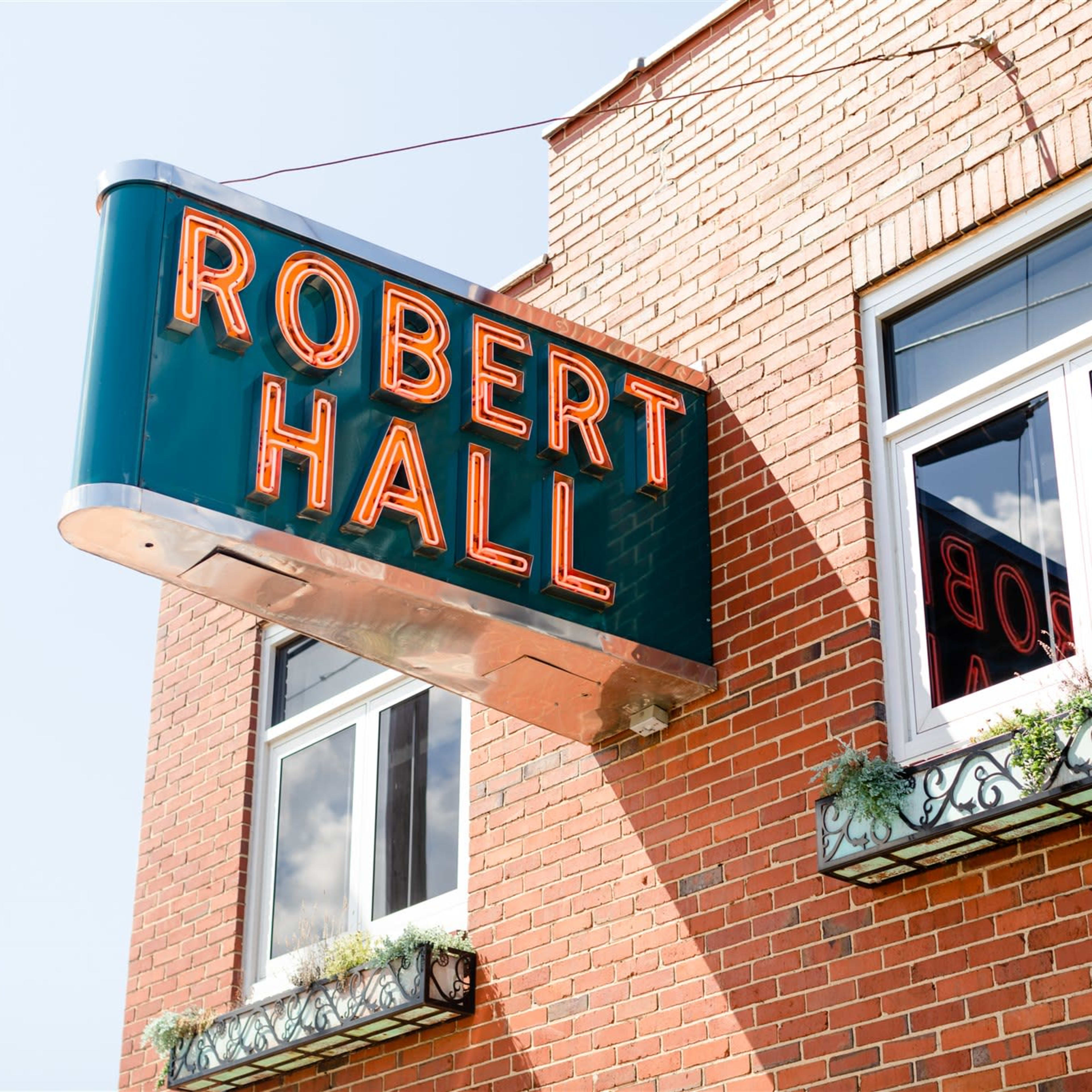 A neon sign reading "ROBERT HALL" hangs above a brick building with window boxes beneath the windows.