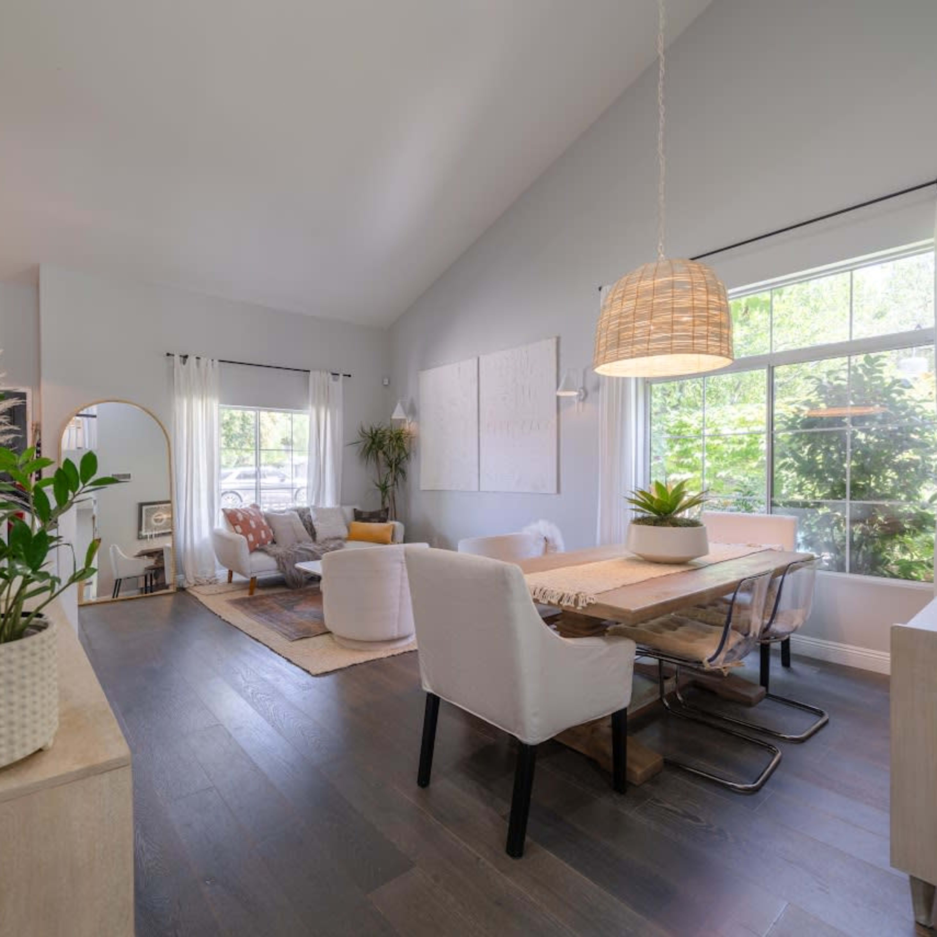 A spacious living area features a dining table, comfortable seating, and large windows allowing natural light to enter.