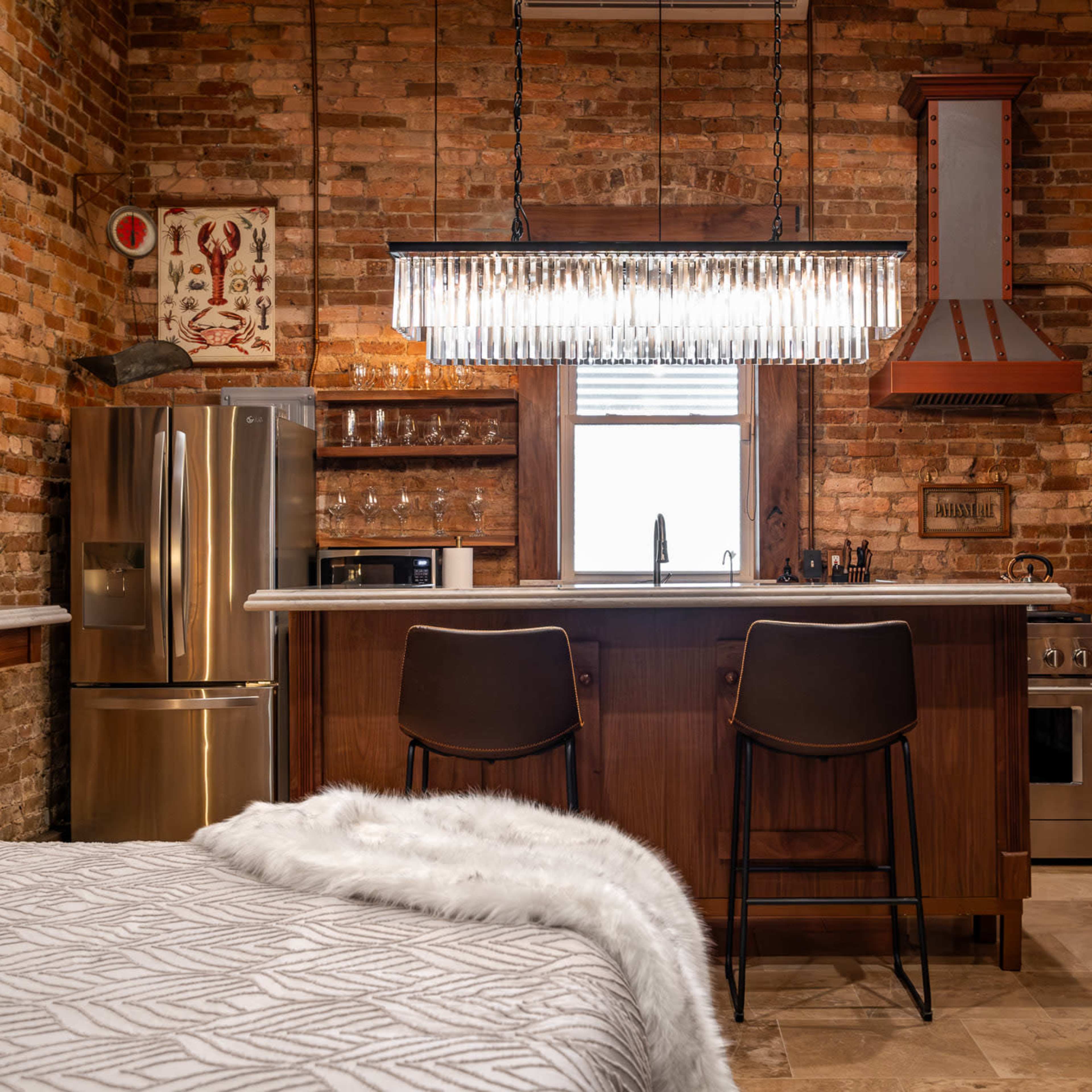 A modern kitchen and dining area characterized by exposed brick walls, a sleek light fixture above a kitchen island, and two bar stools.