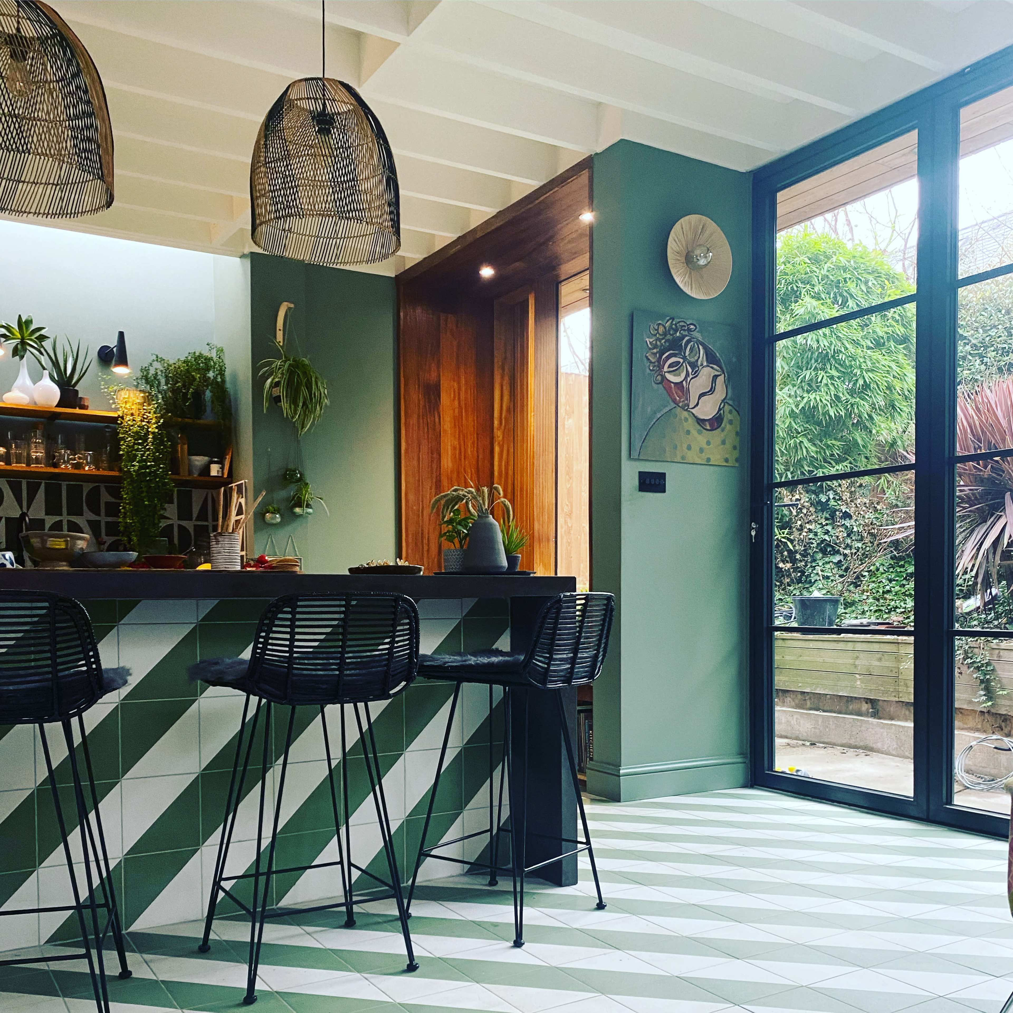A modern kitchen with a green and white tiled floor, a bar area with black bar stools, and large glass doors leading to an outdoor space.