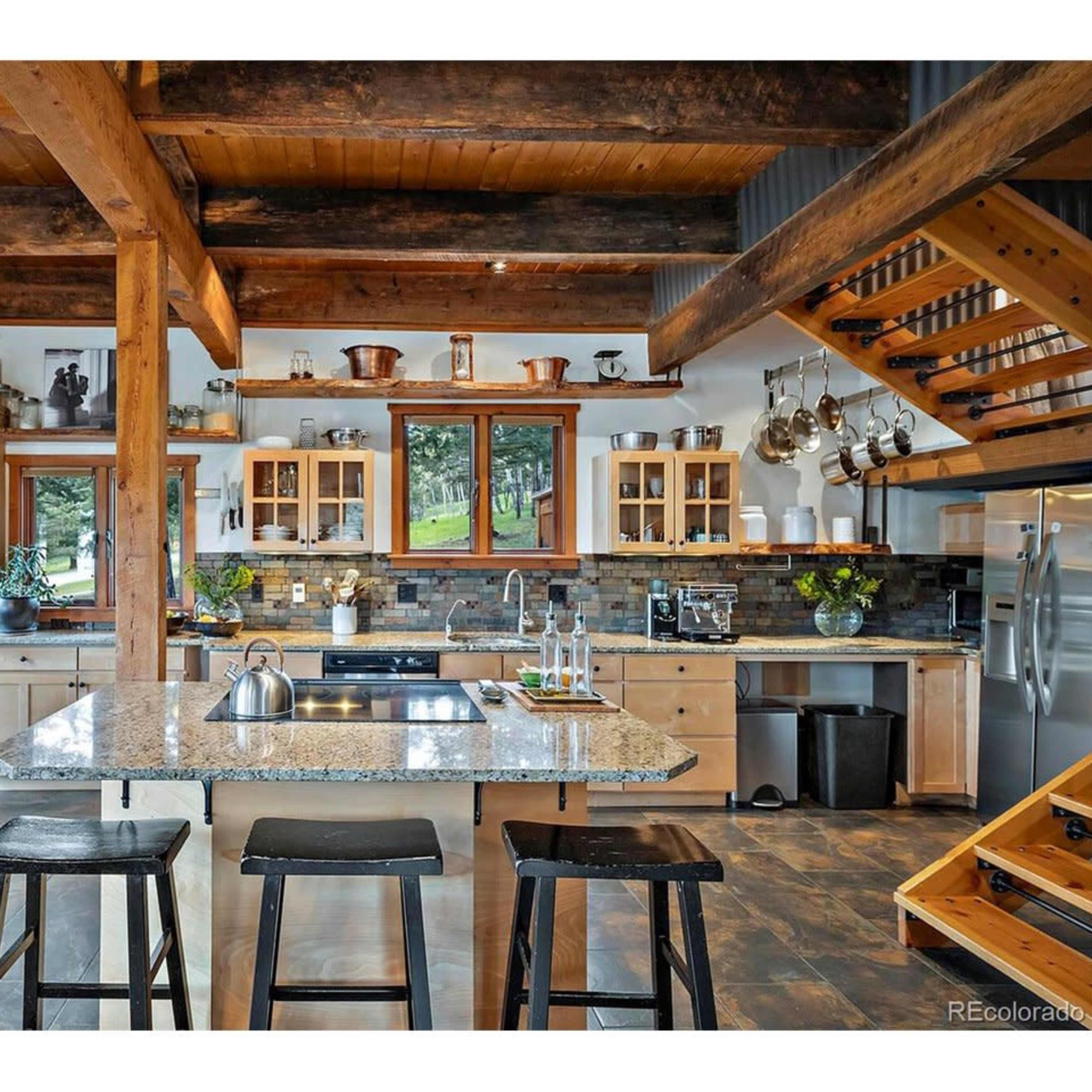 A modern kitchen features wooden beams, a central island with seating, and various kitchen appliances and utensils arranged on shelves.