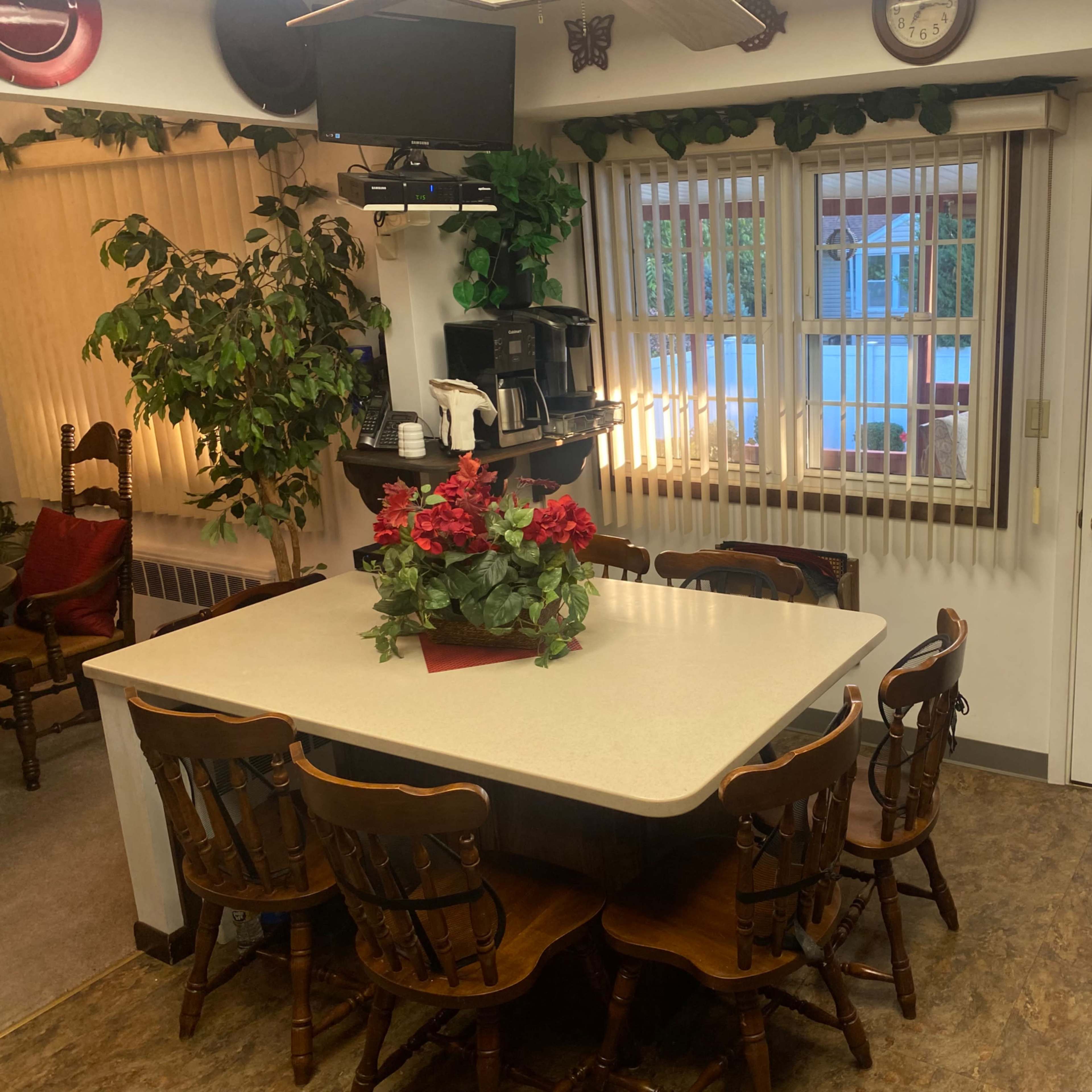 A dining area features a large table surrounded by eight wooden chairs, with a coffee station and a door leading outside.