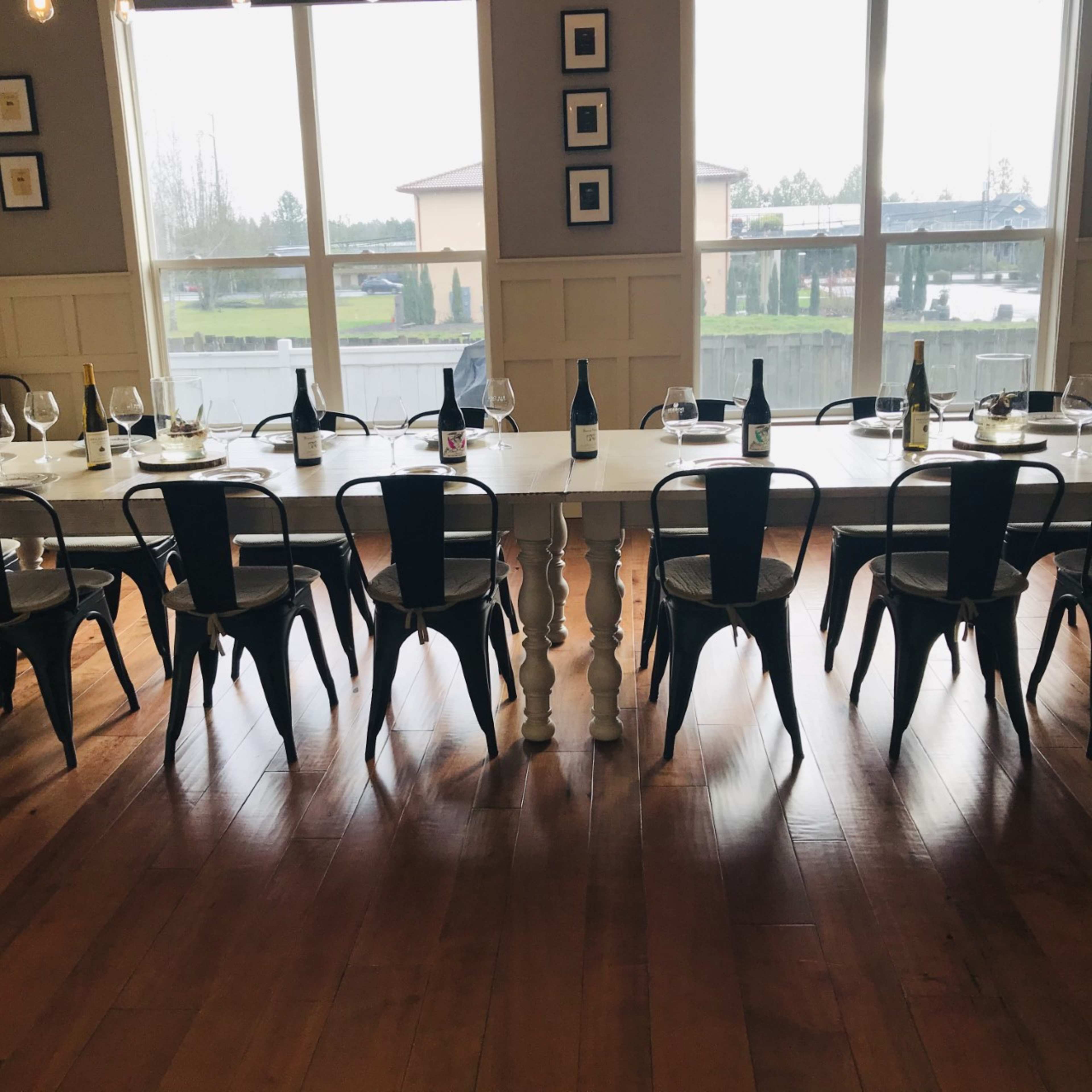A long table set for a tasting is flanked by metal chairs, with several wine bottles and glasses arranged neatly on the table.