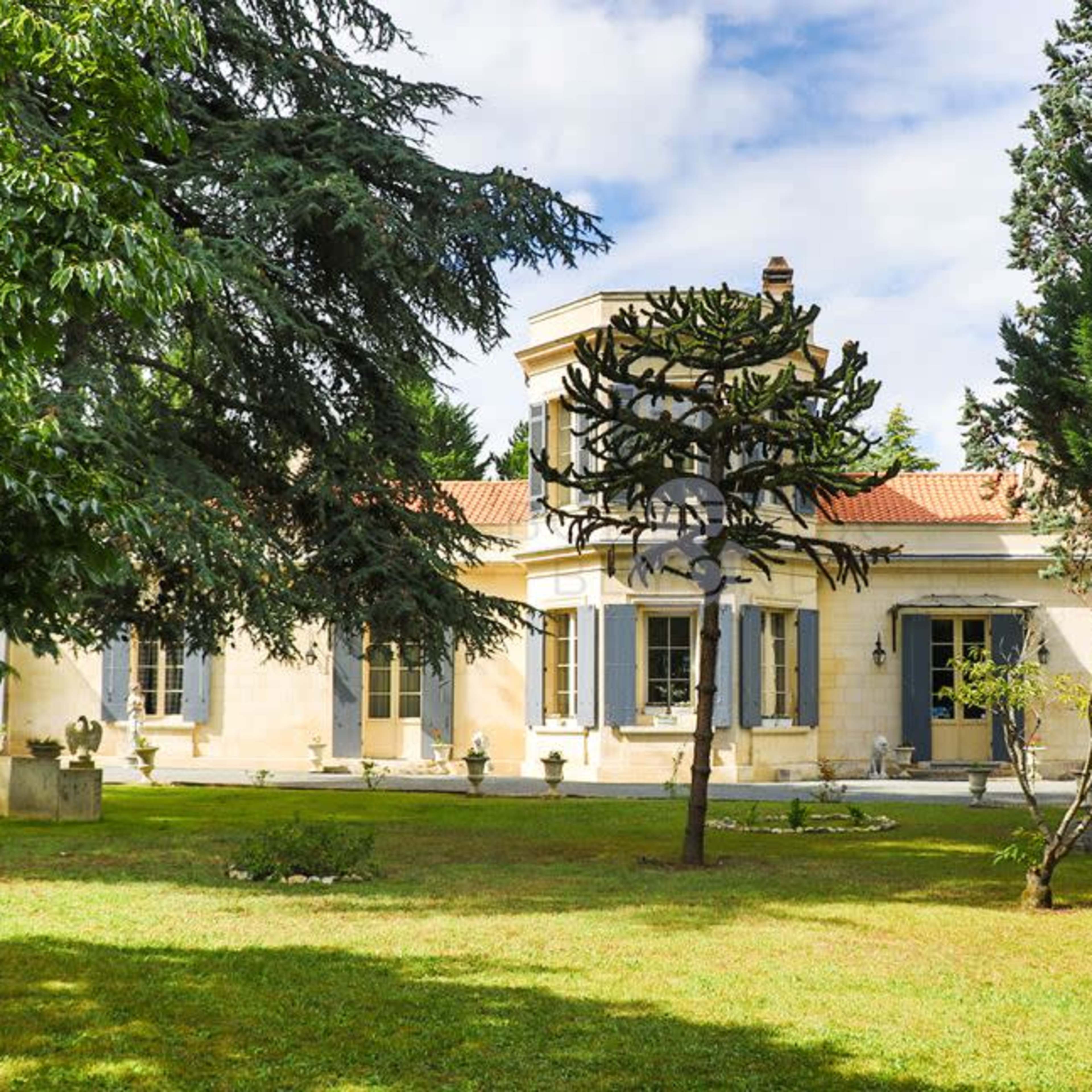 A large, single-story house with a manicured lawn and tall trees surrounding it.