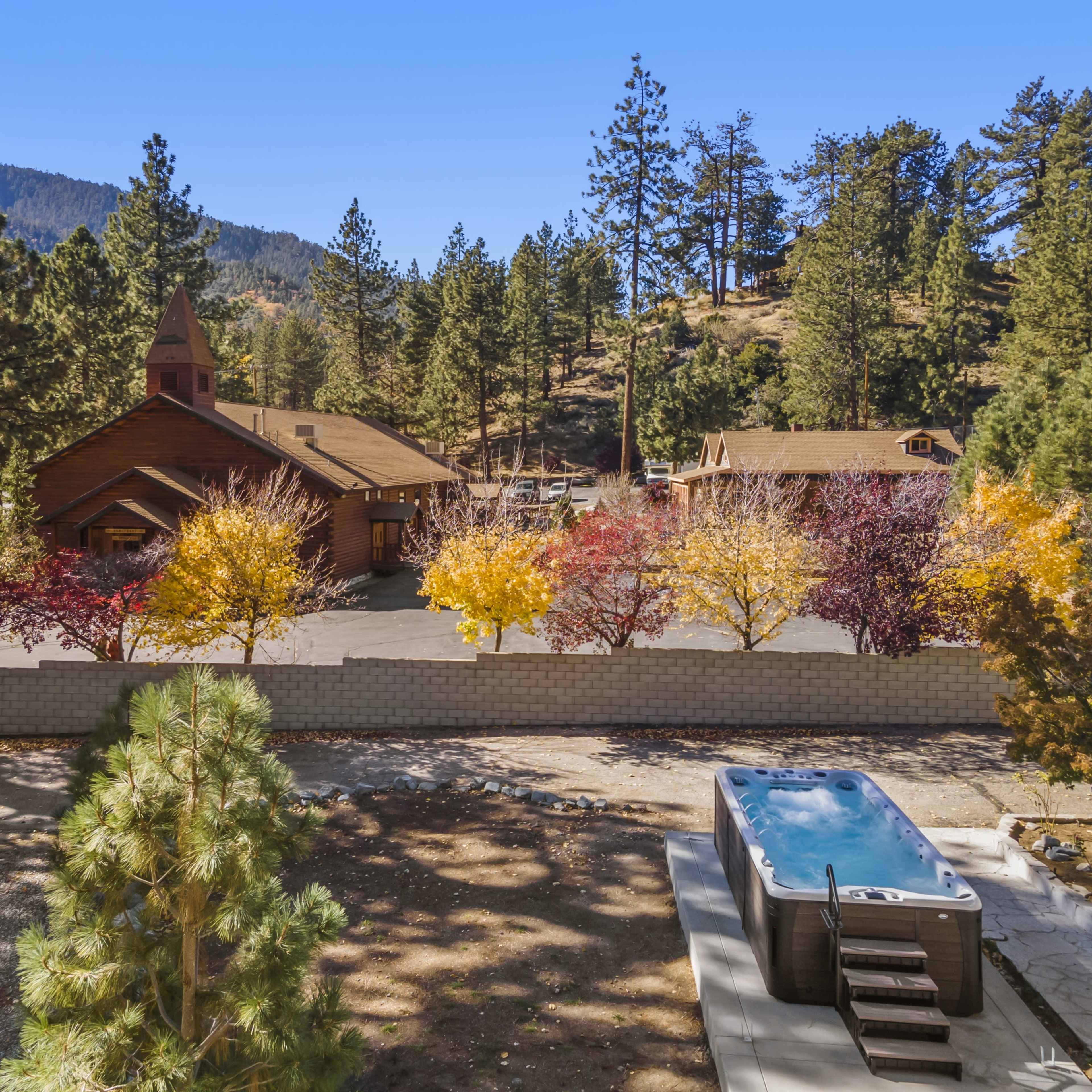 A peaceful mountain scene featuring a lodge-style building surrounded by colorful trees and a hot tub in the foreground.