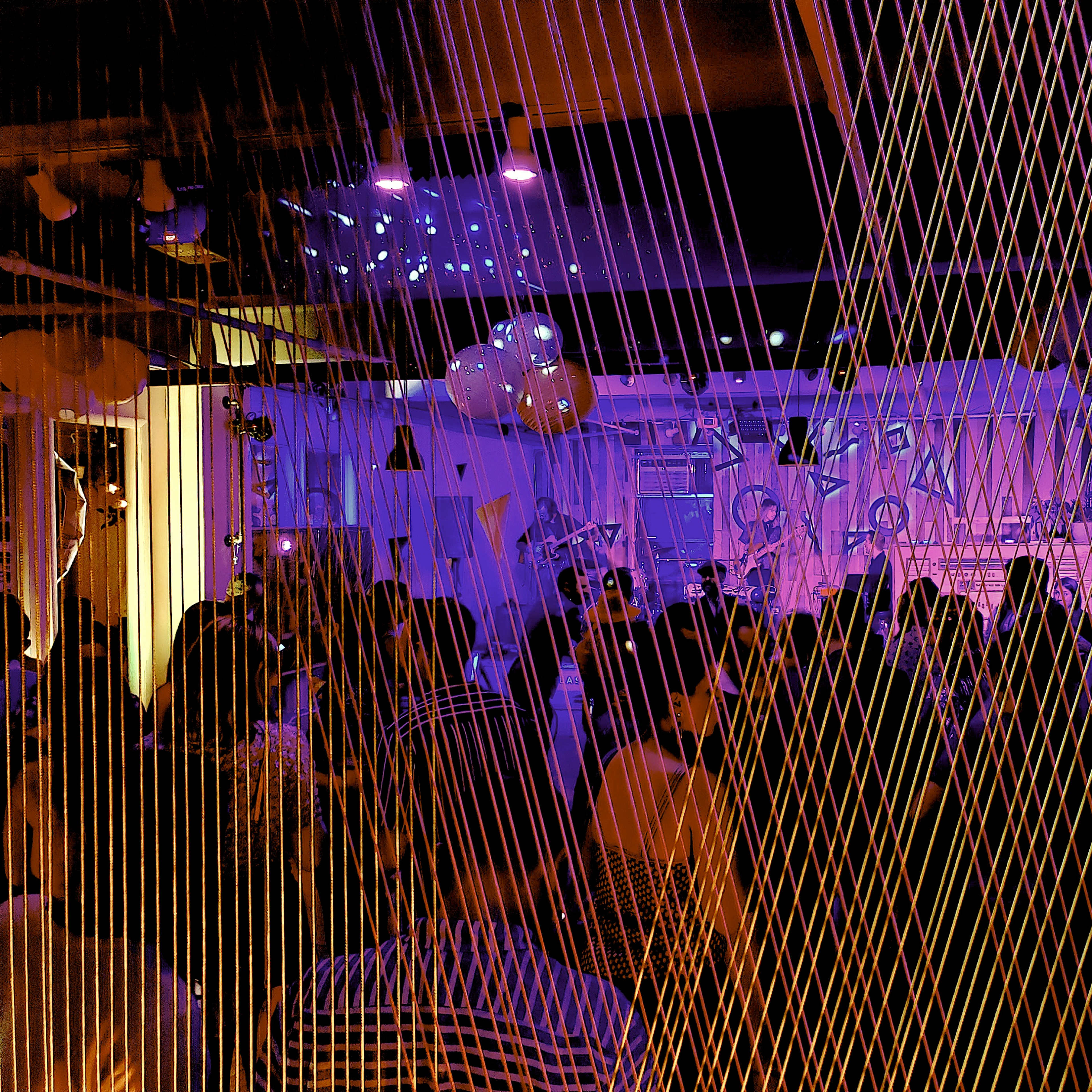 A crowd gathers in a dimly lit venue decorated with colorful lighting and geometric patterns.