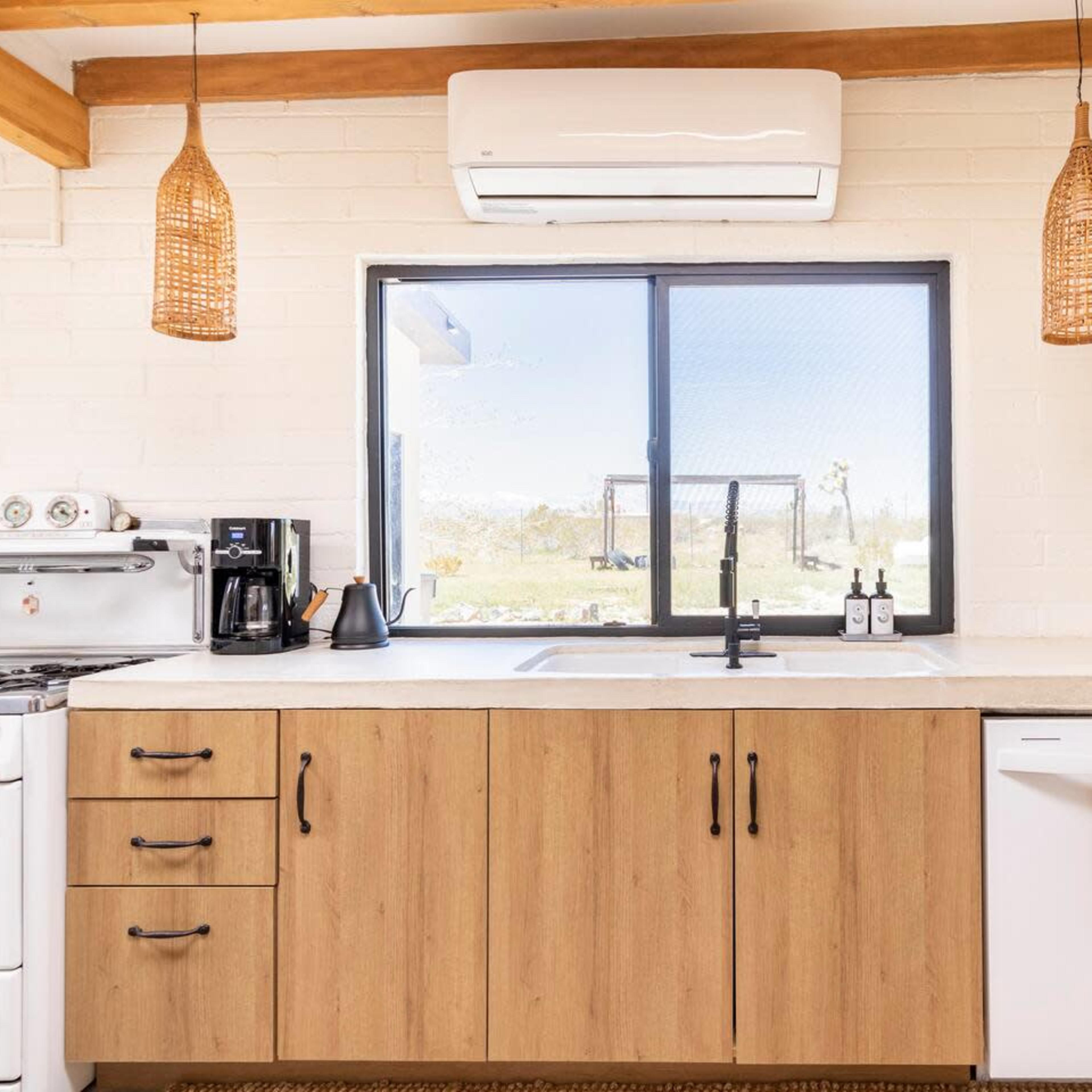A modern kitchen features a wooden cabinet setup, a sink with a black faucet, and large windows overlooking a landscaped outdoor area.