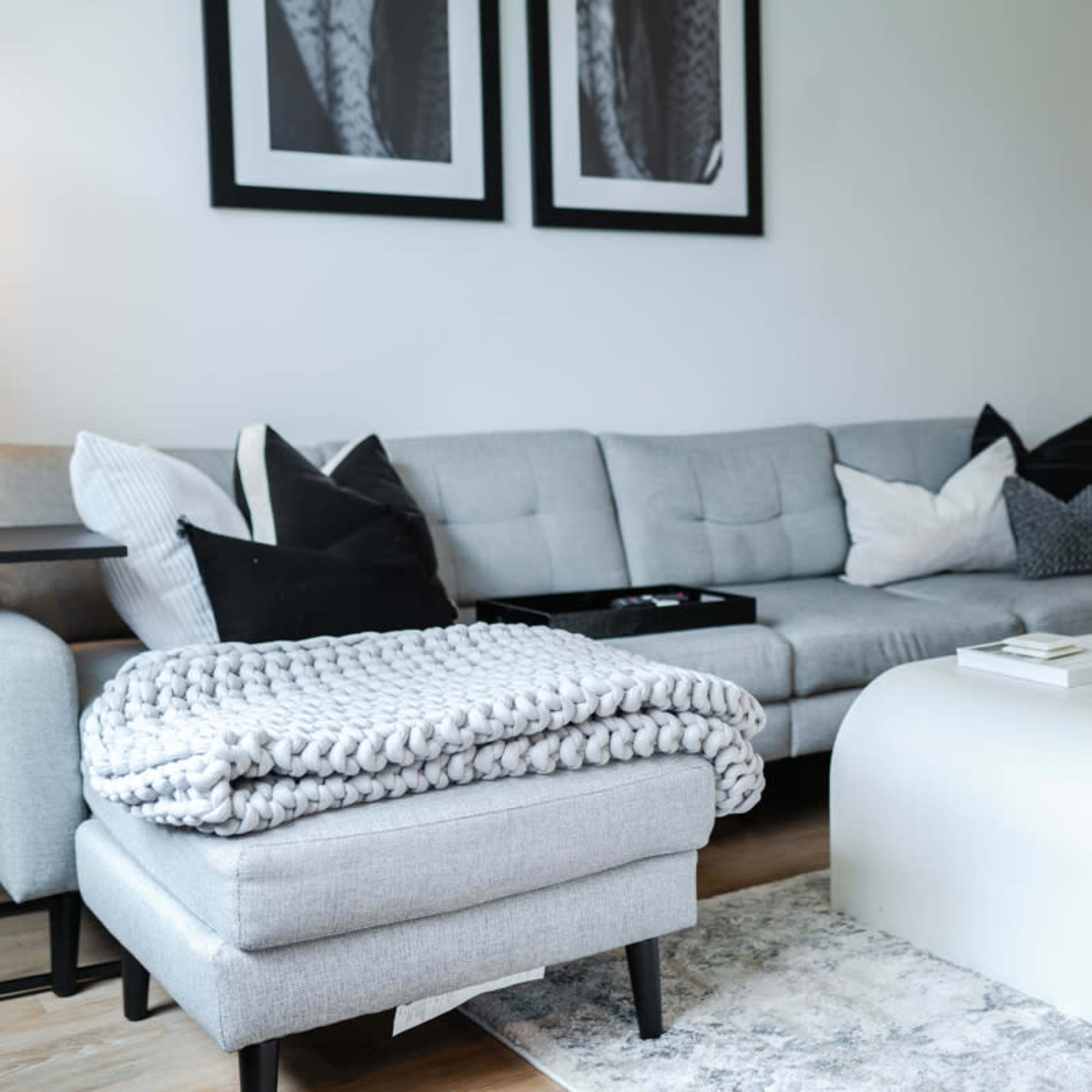 A modern living room featuring a gray sofa with decorative pillows, a white coffee table, and a cozy throw blanket draped over an ottoman.