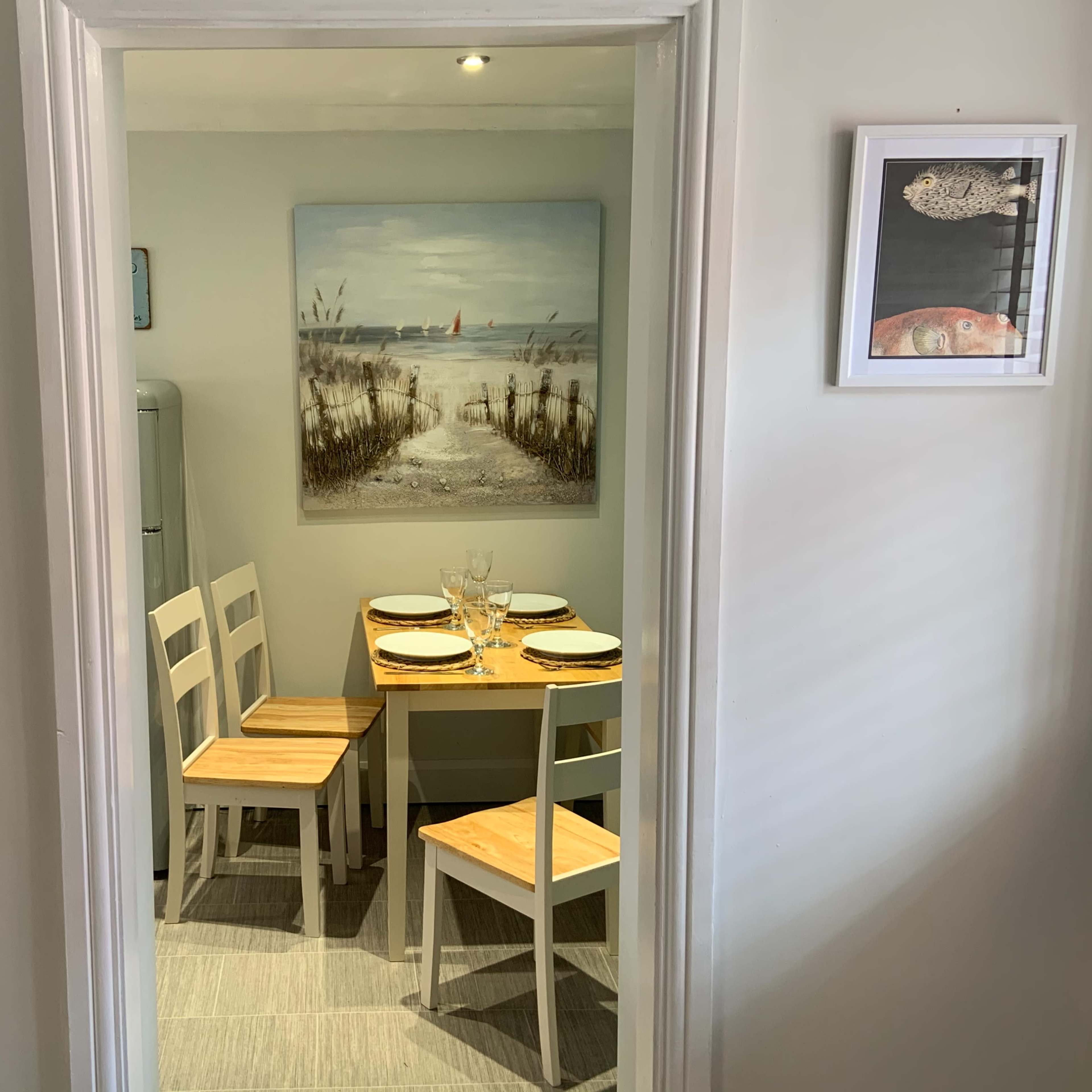 A small dining area features a table with four chairs and a painting of a beach scene on the wall.
