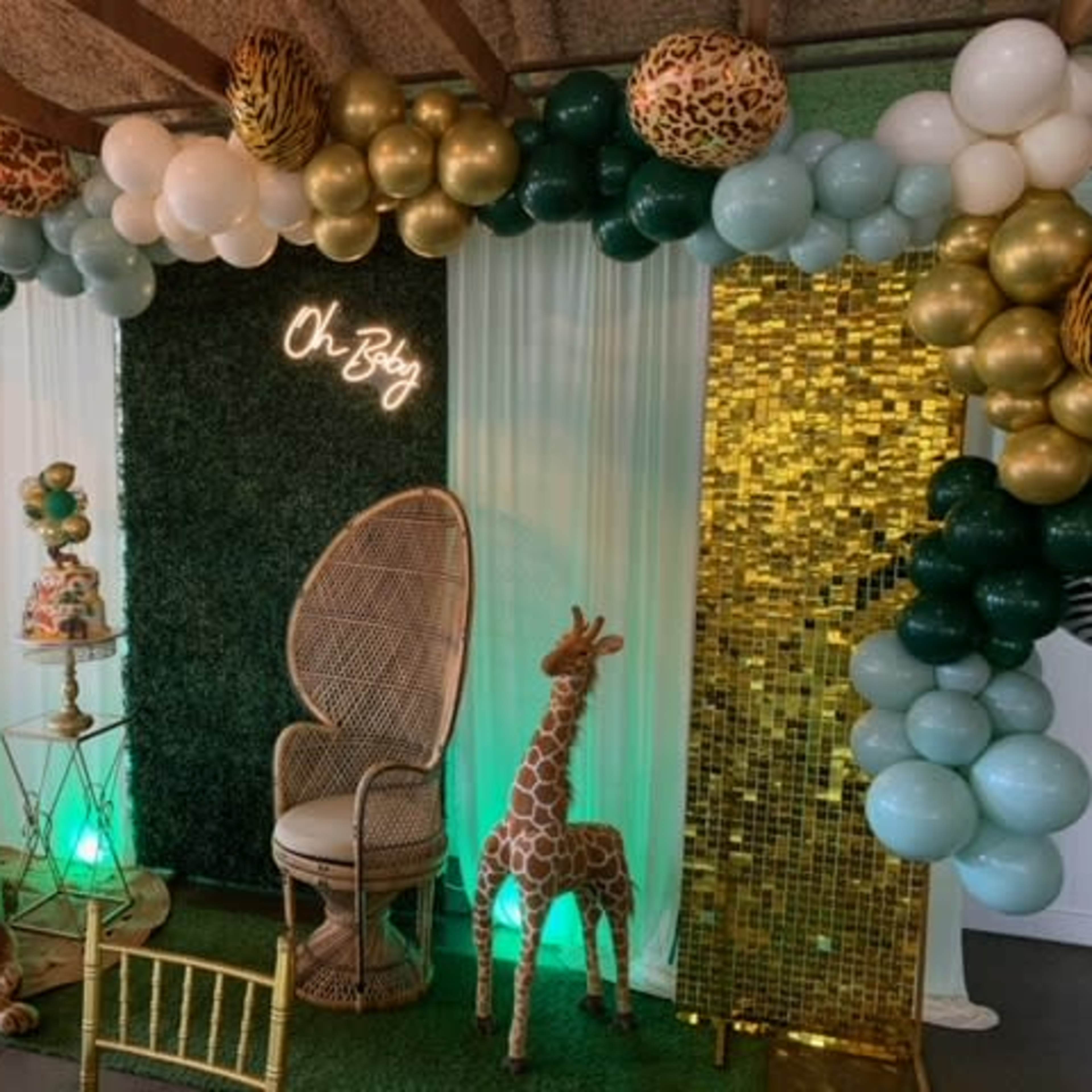 A decorated party area featuring a large balloon arch, a decorative chair, a cake table, and themed props including a giraffe and a lion.