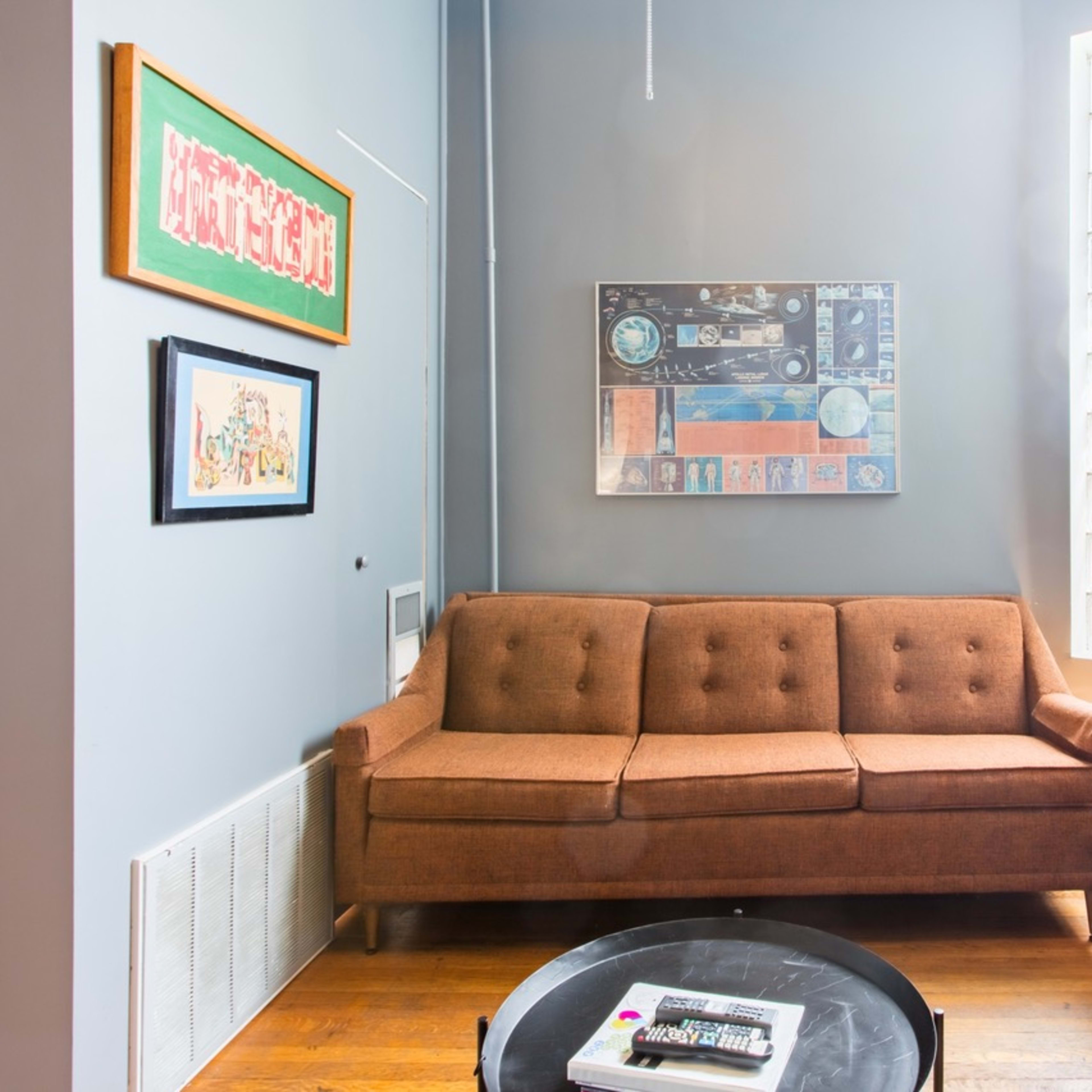 A cozy living room featuring a brown sofa, a glass block window, and a round coffee table with magazines.