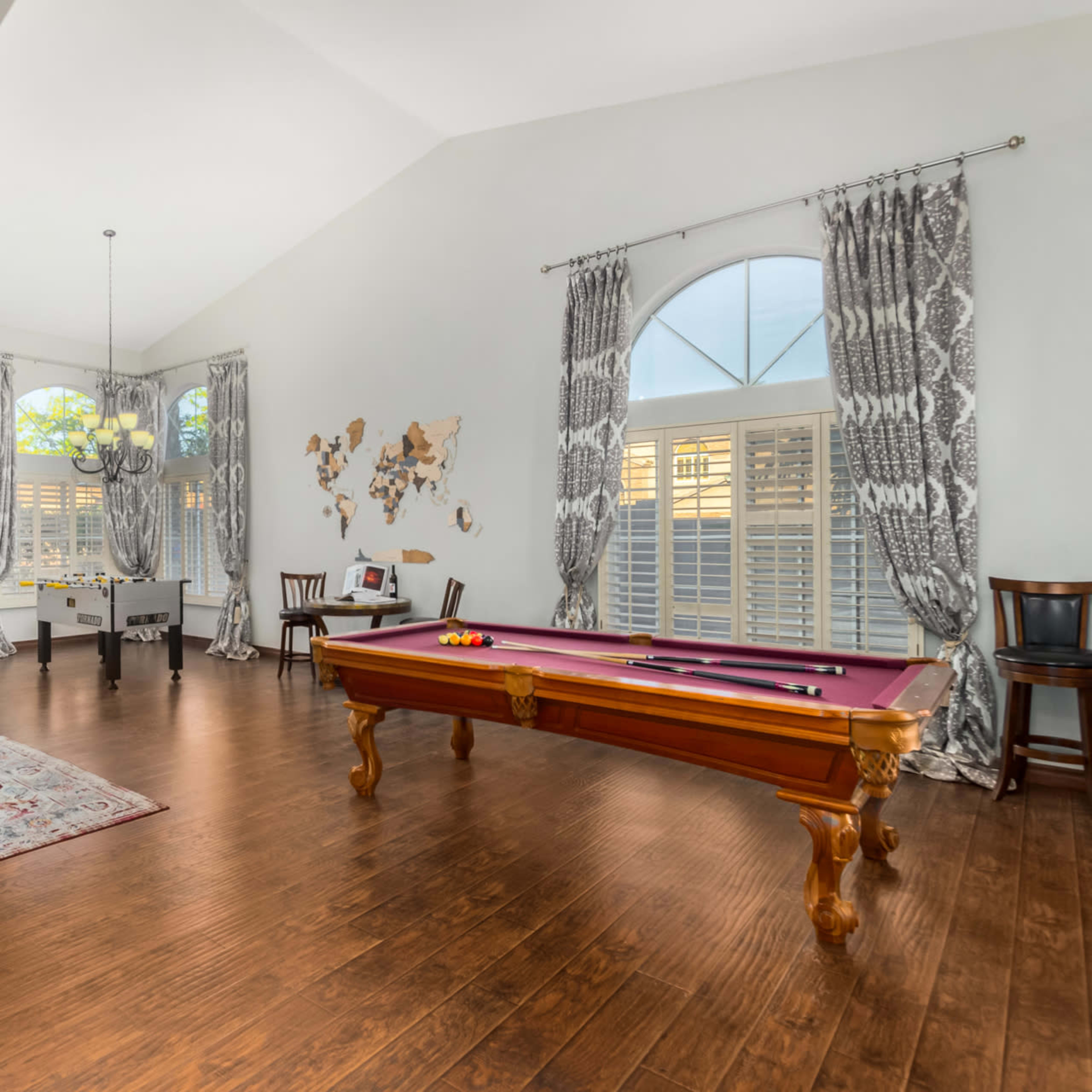 The room features a pool table, a large decorative mirror, and a world map on the wall, with elegant curtains framing the windows.
