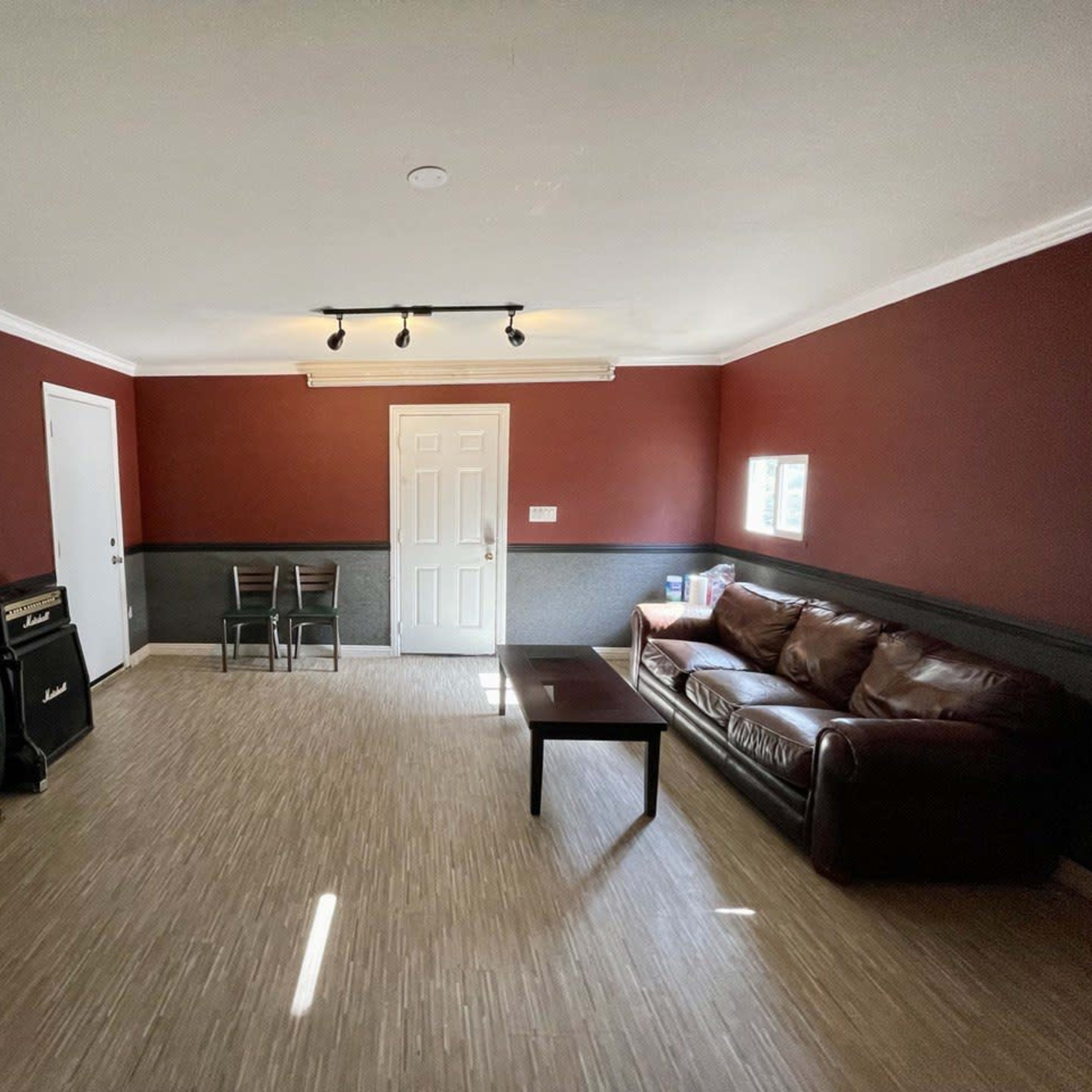 The room features dark red walls, a brown leather couch, a coffee table, and musical instruments in one corner.