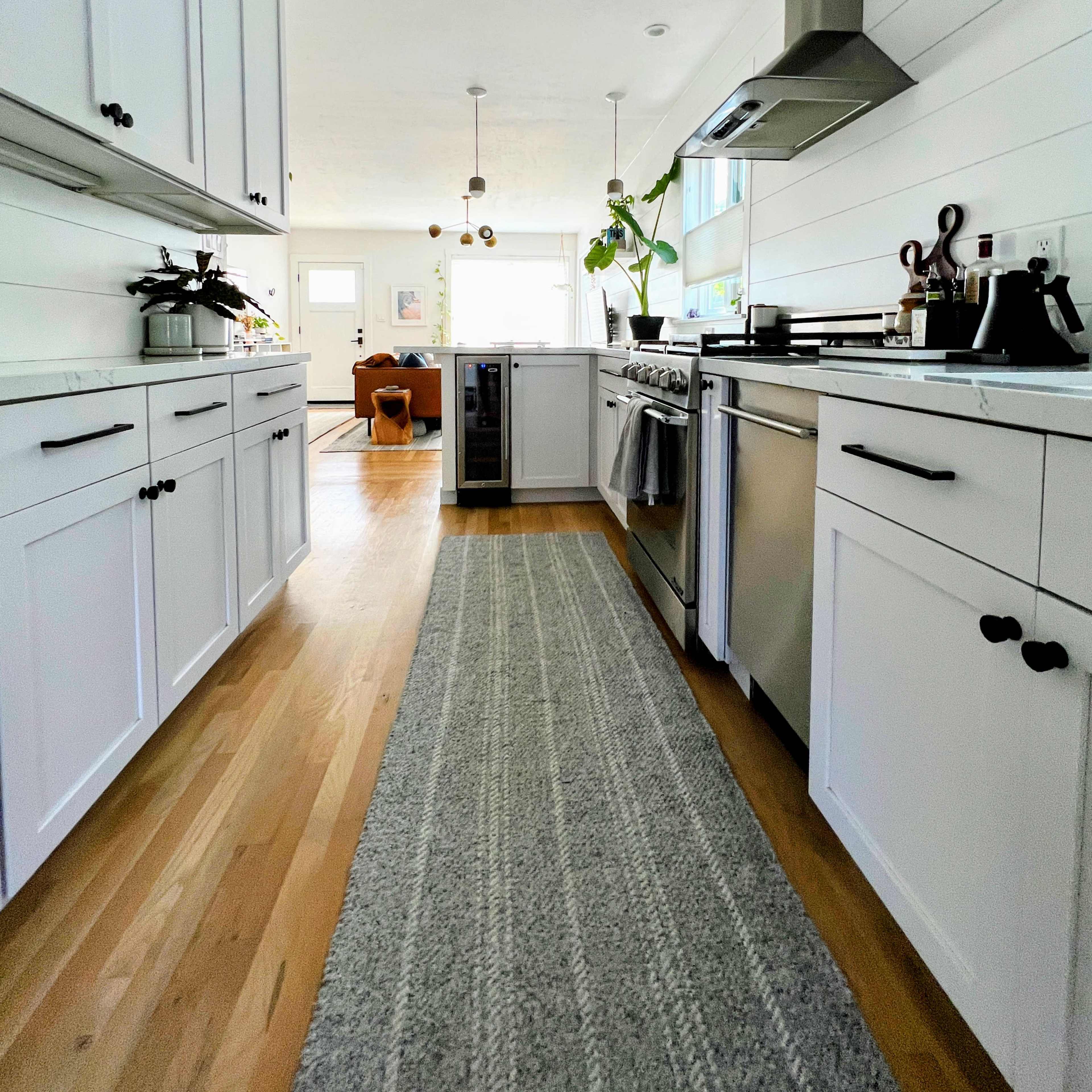 A modern kitchen with white cabinetry, stainless steel appliances, and a center island, featuring a rug running down the wooden floor.