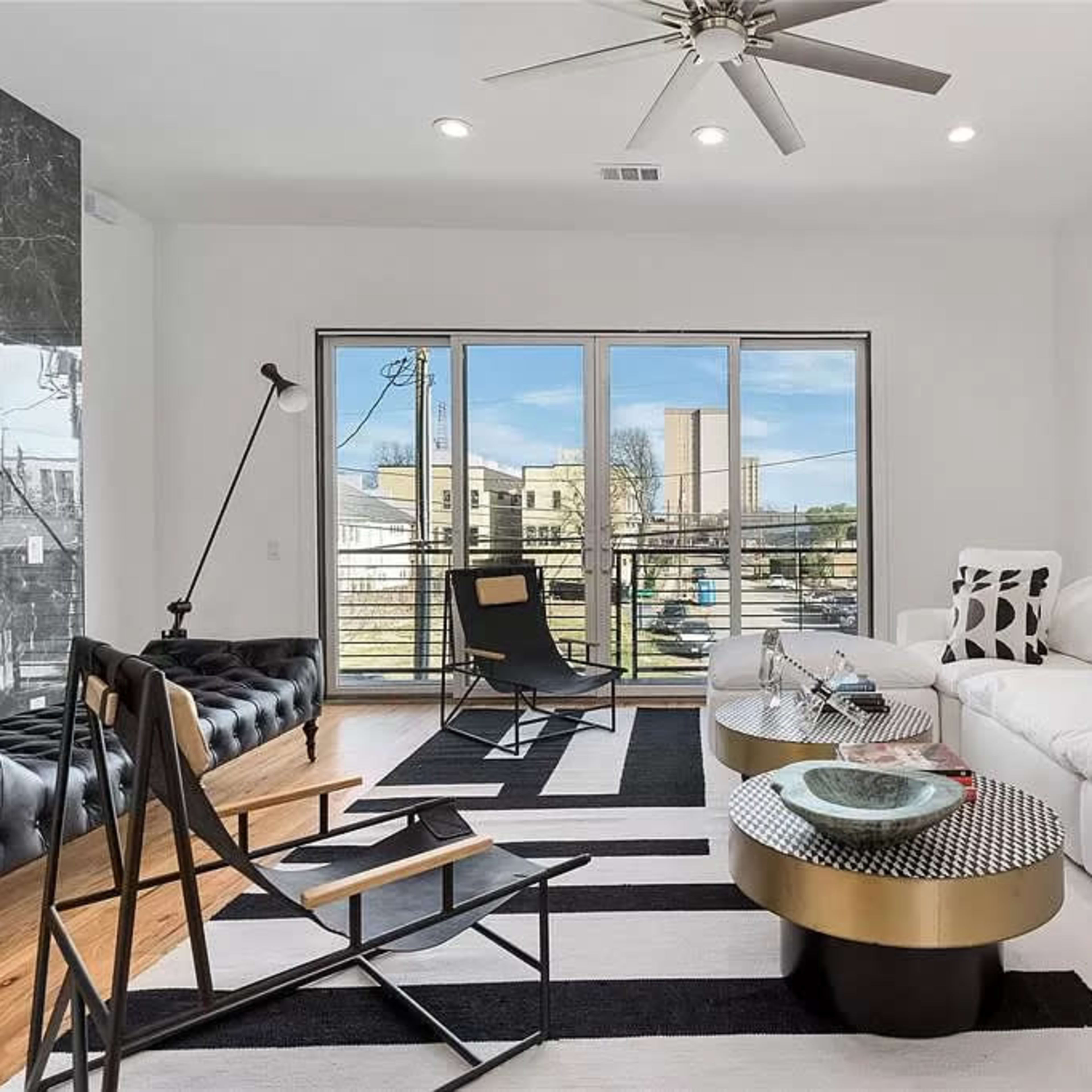 A modern living room featuring a white sofa, black and white patterned rug, and large windows that provide outdoor views.