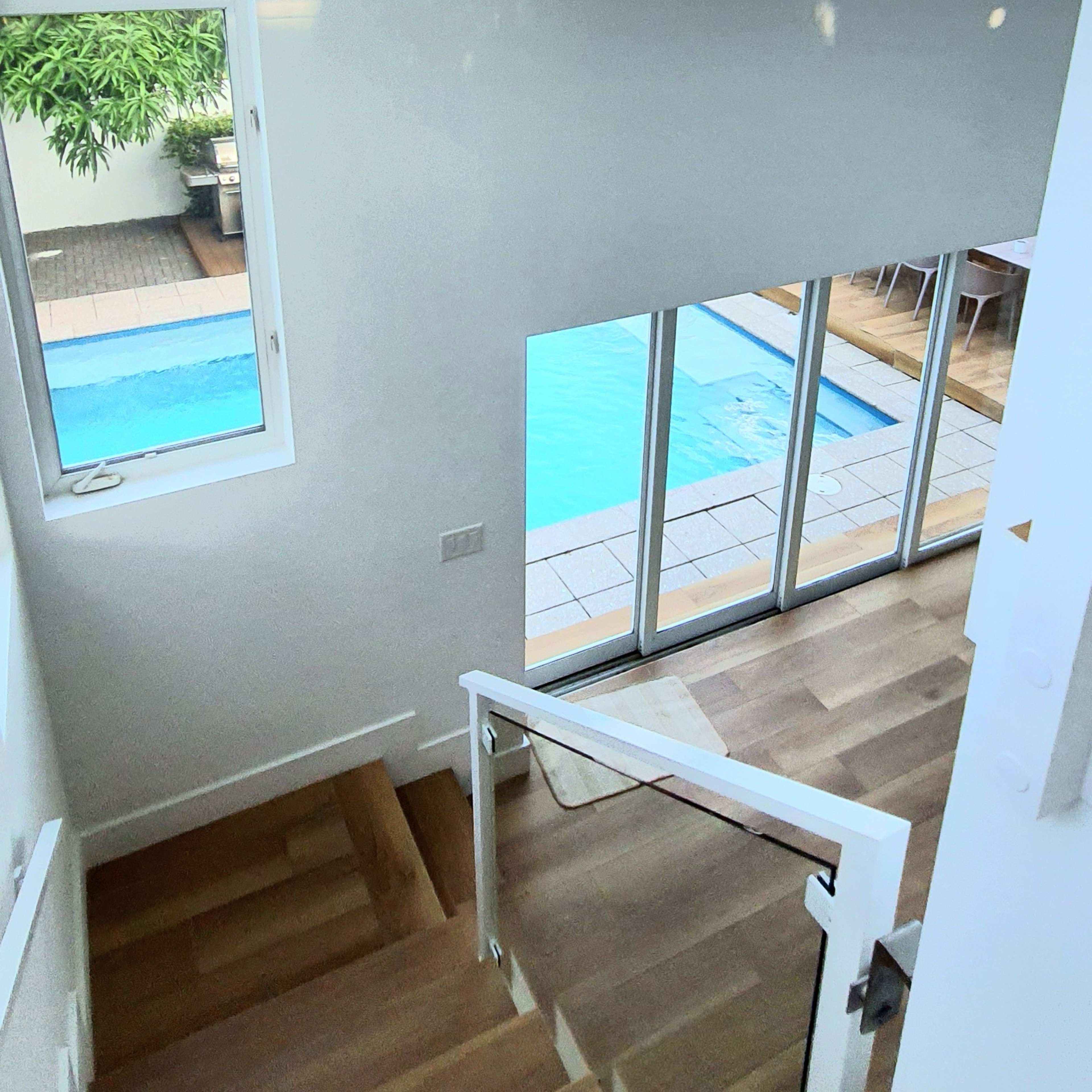 A modern interior staircase leading down to a spacious living area with large windows overlooking a pool and outdoor space.