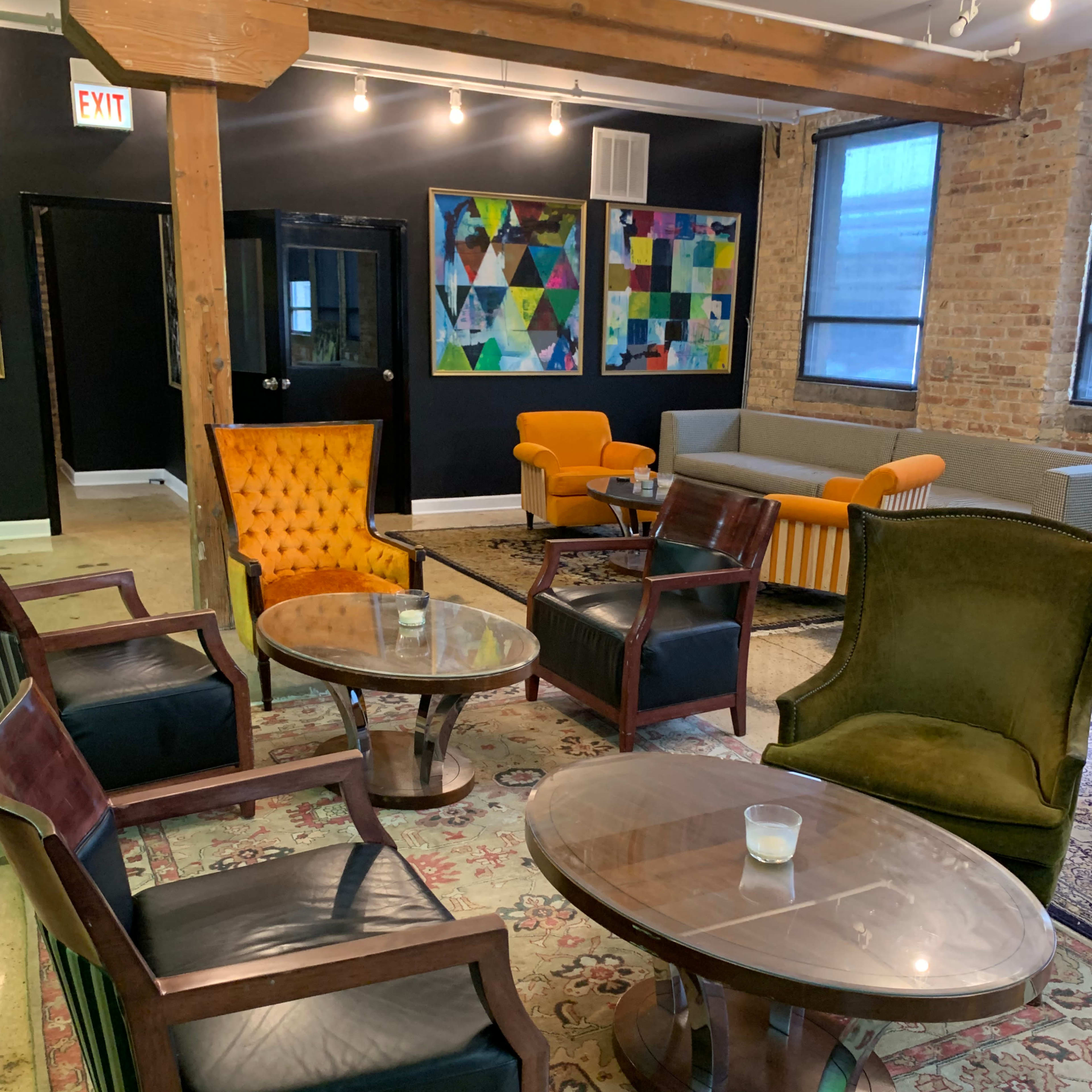 A cozy lounge area features various seating options, including colorful armchairs and a patterned rug, with distinct artwork on the walls.