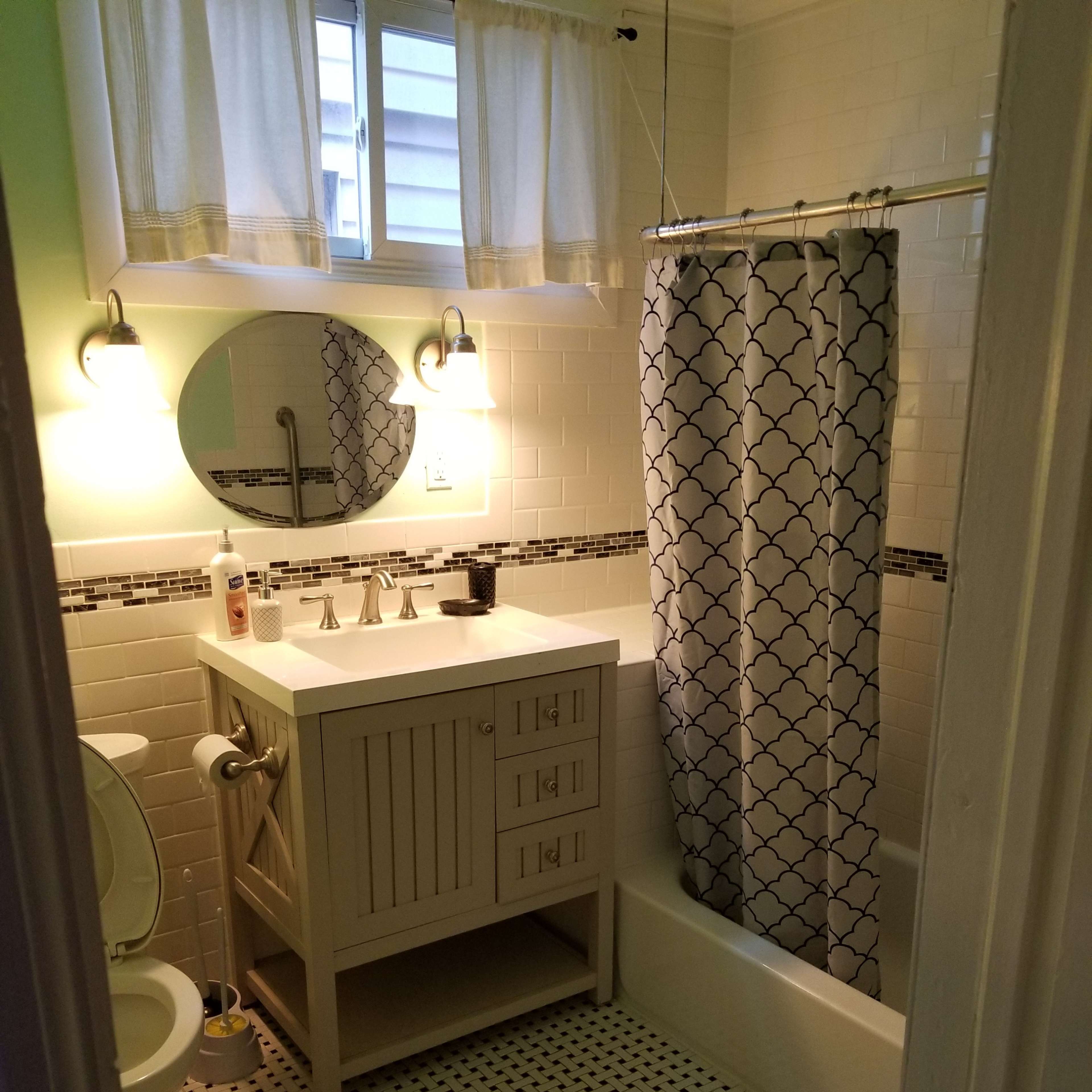 A small bathroom featuring a white tub with a shower curtain, a rectangular vanity with a sink, and a toilet with patterned tile flooring.