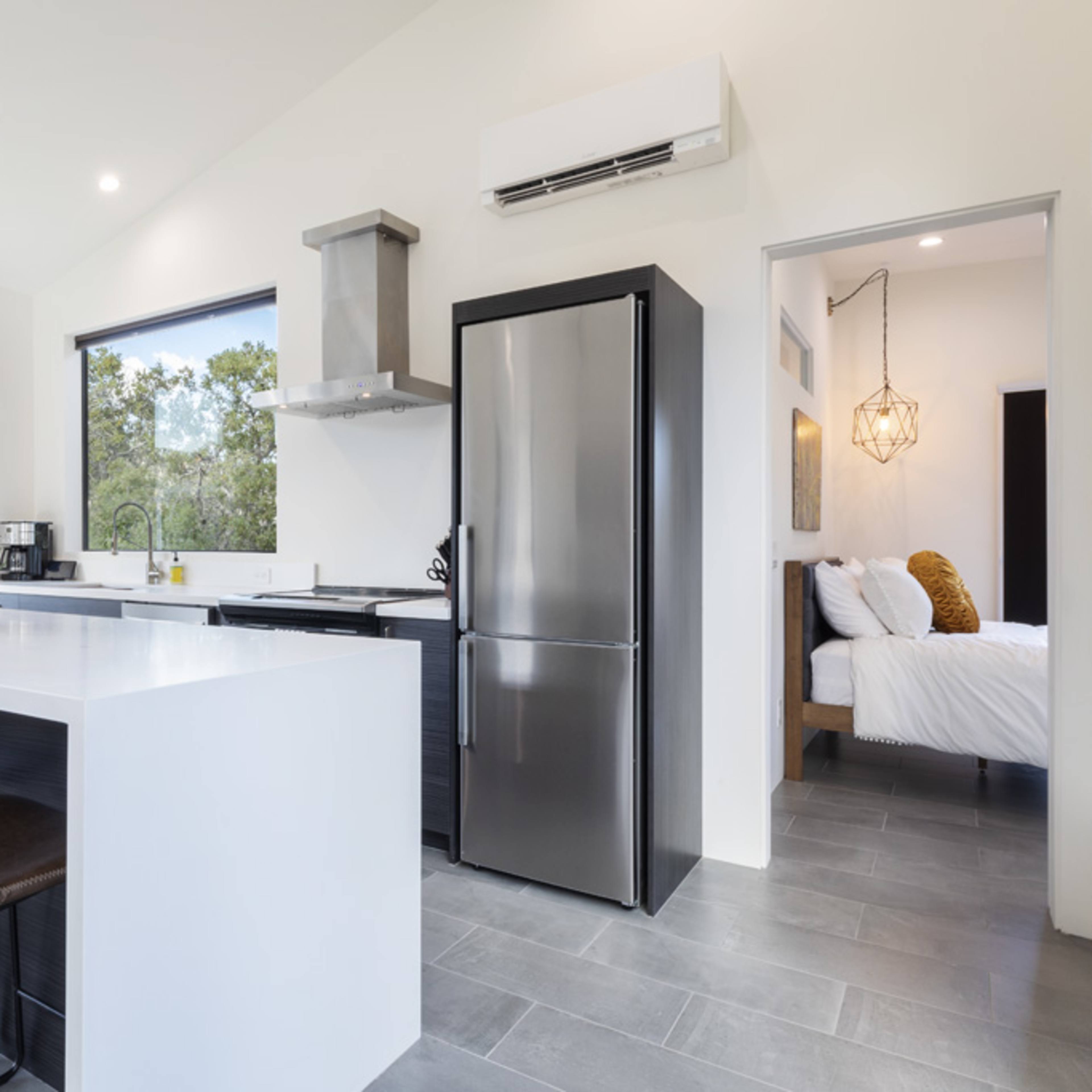 A modern kitchen with a white island counter, black appliances, and large windows overlooking a mountainous landscape.