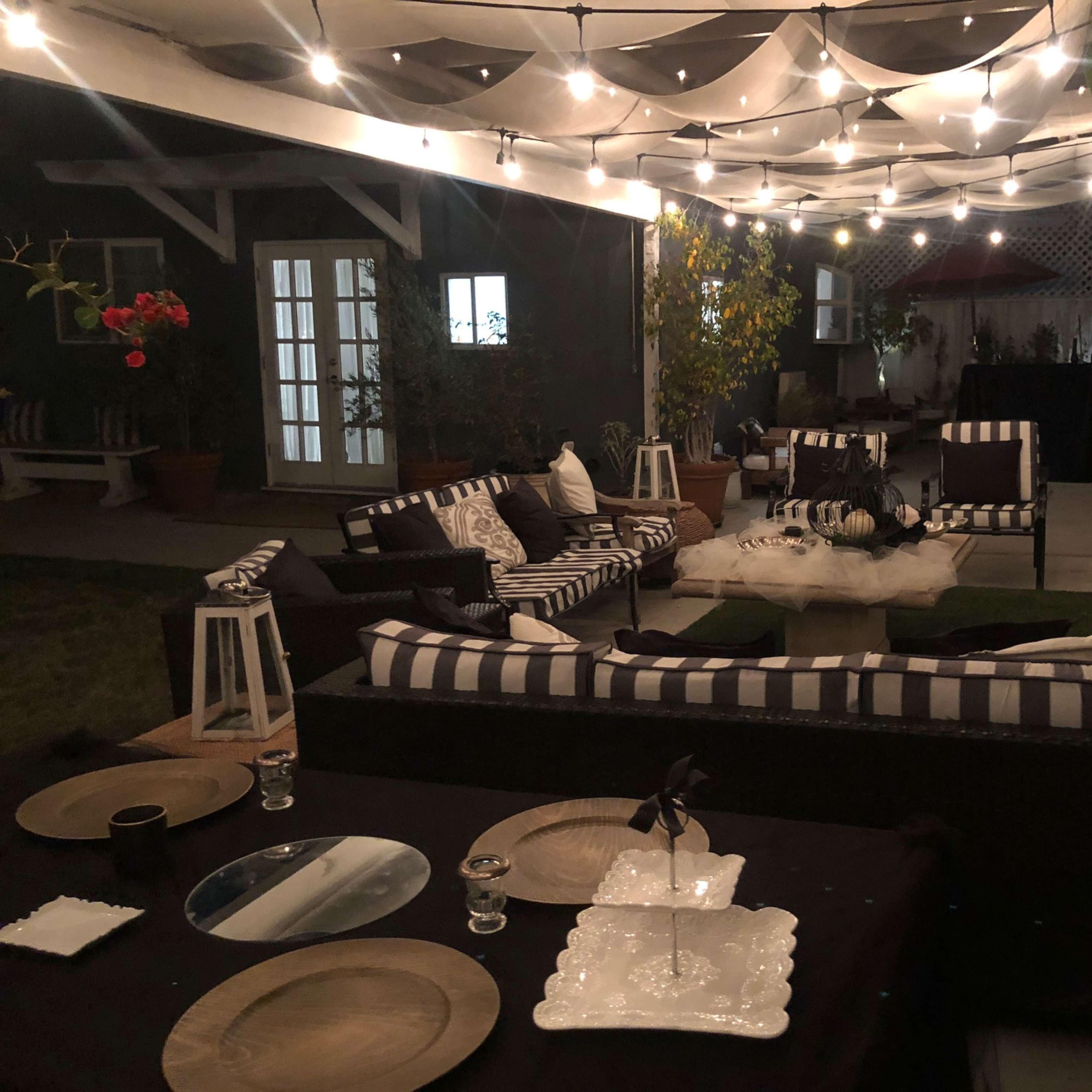 A cozy outdoor seating area with striped cushions, decorative lanterns, and string lights hanging overhead.