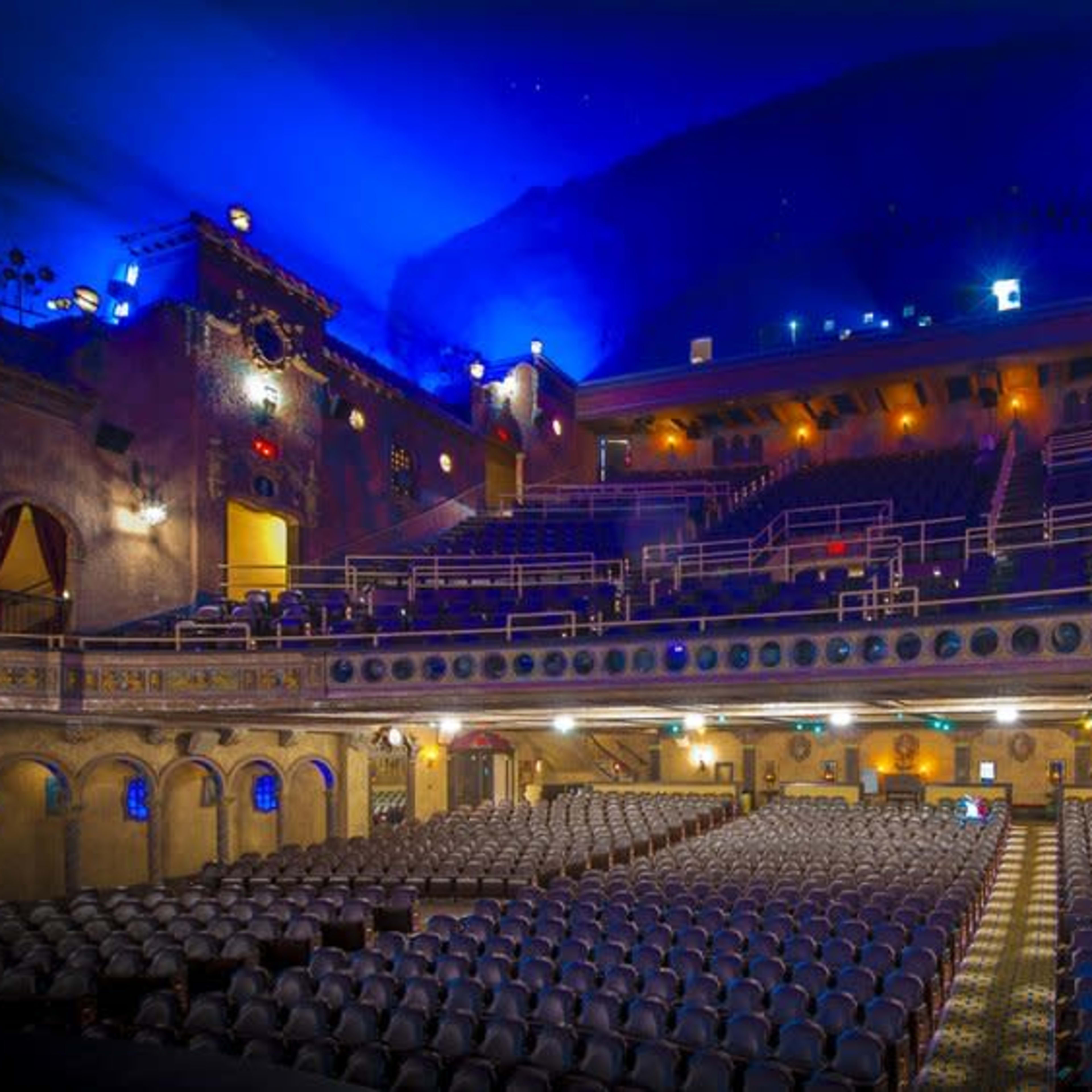 An empty theater with rows of seats, ornate architectural details, and a blue-lit ceiling.