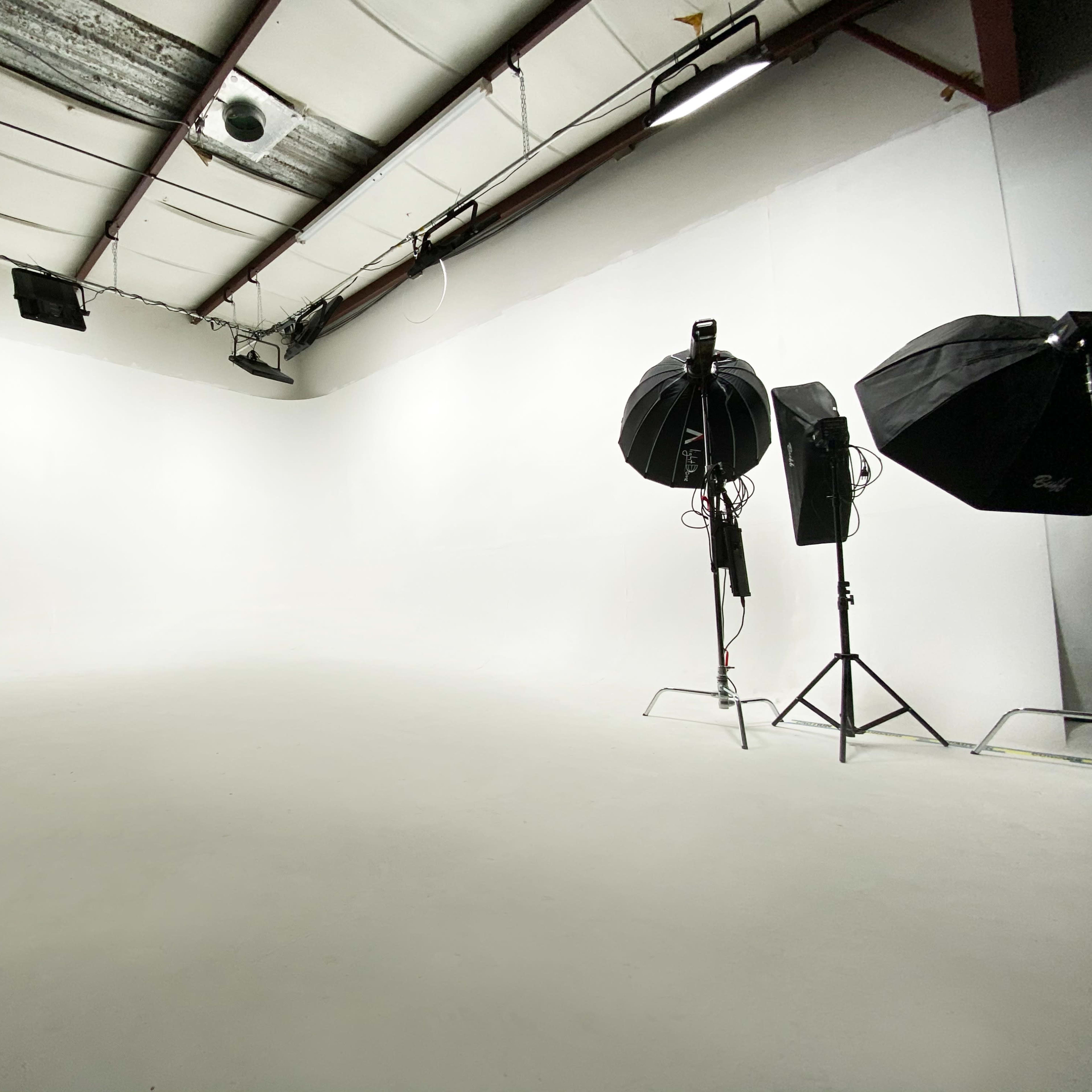 A spacious, empty photography studio with white walls and two lighting setups on stands.