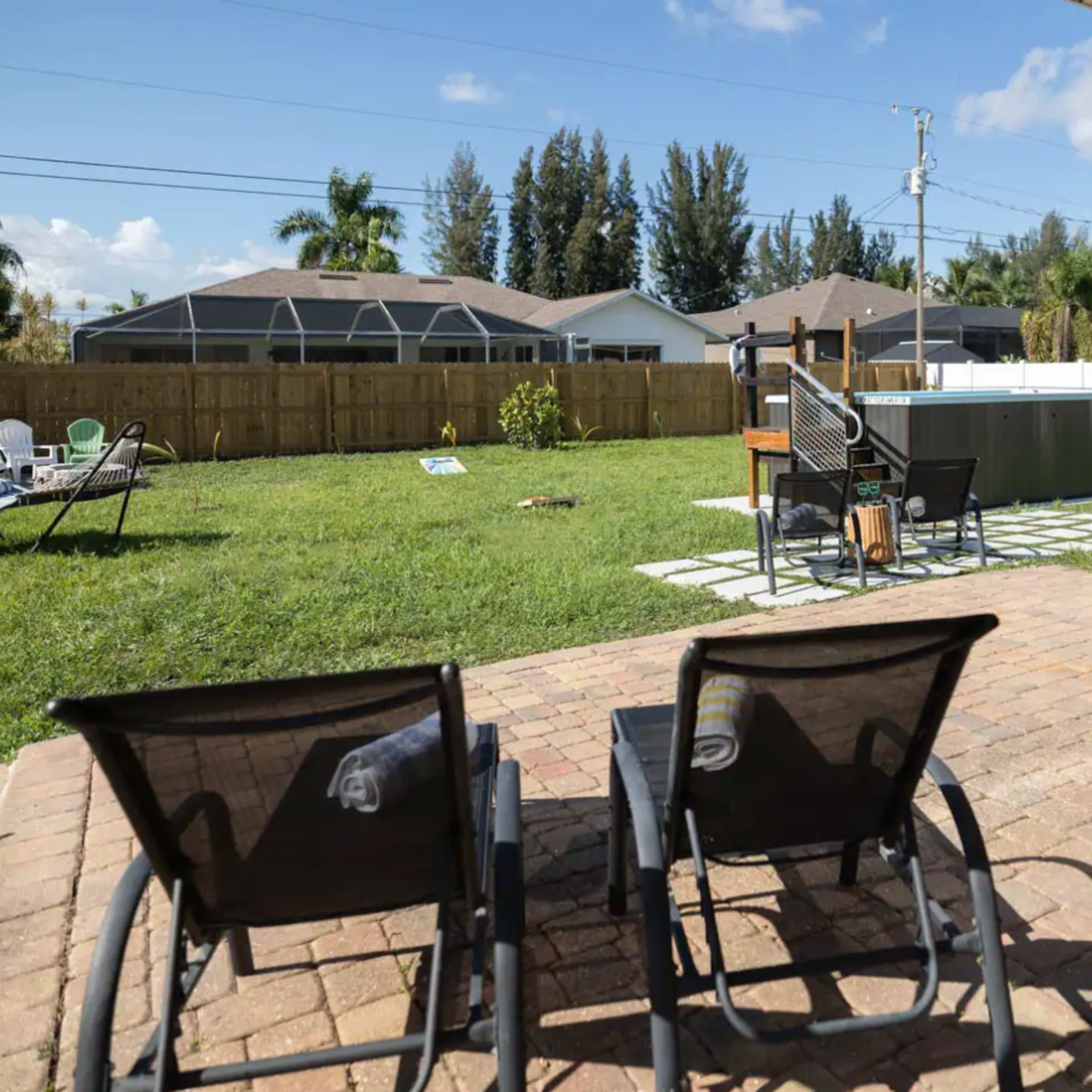 A backyard with two lounge chairs in the foreground, overlooking a grassy area with a children's play set and a pool in the background.
