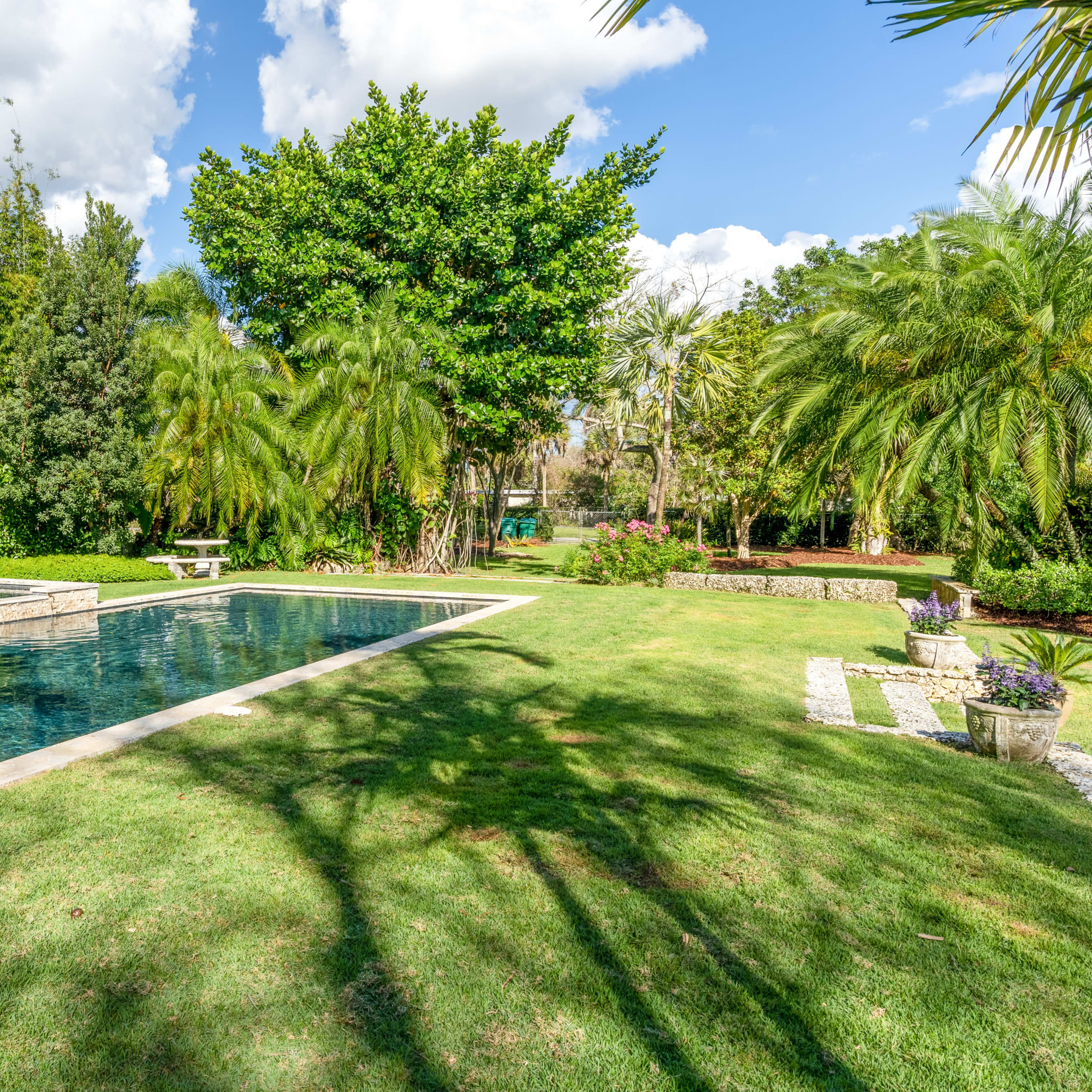 A neatly landscaped backyard features a swimming pool surrounded by lush greenery and various trees.
