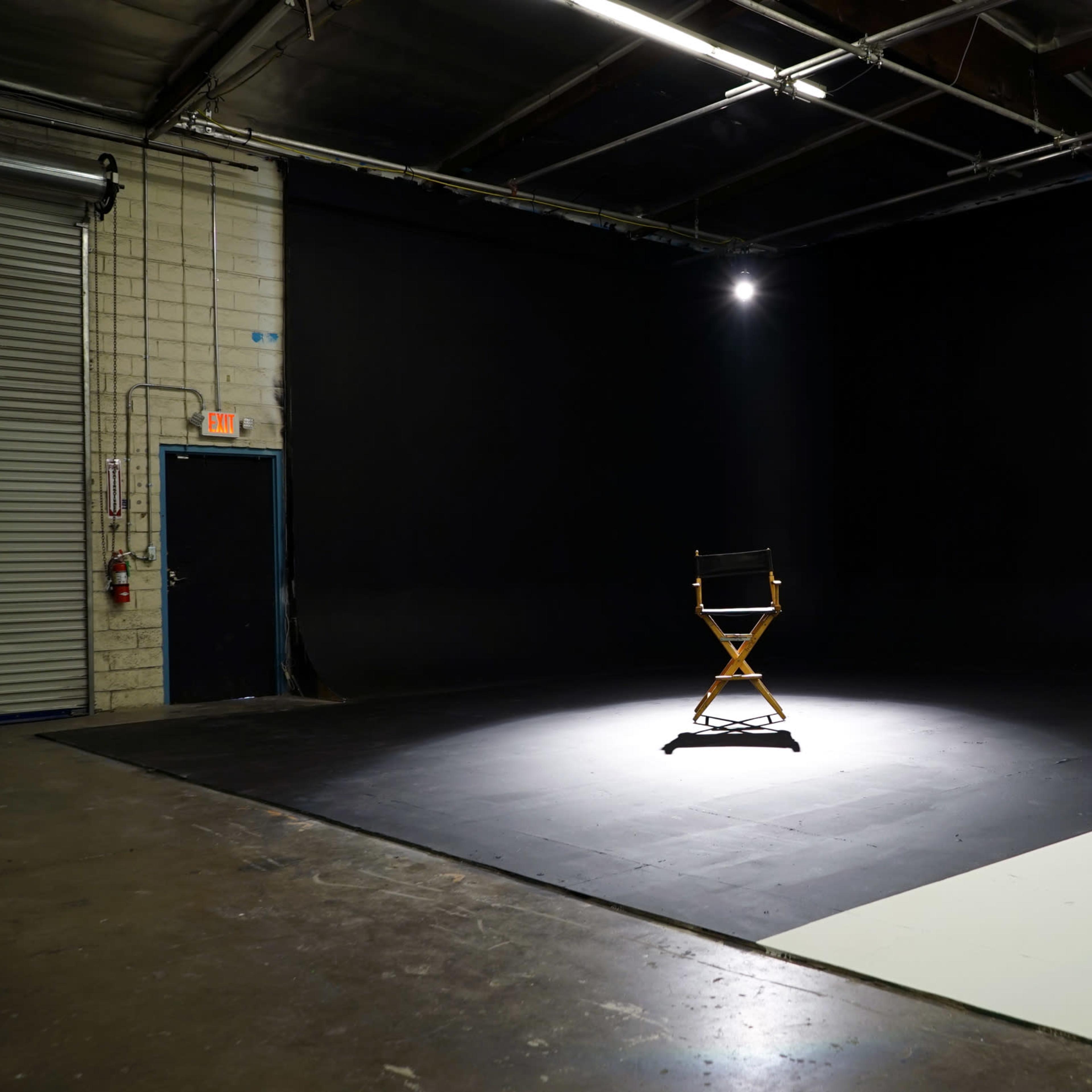 A single director's chair is illuminated in a dark studio space with a gray backdrop.