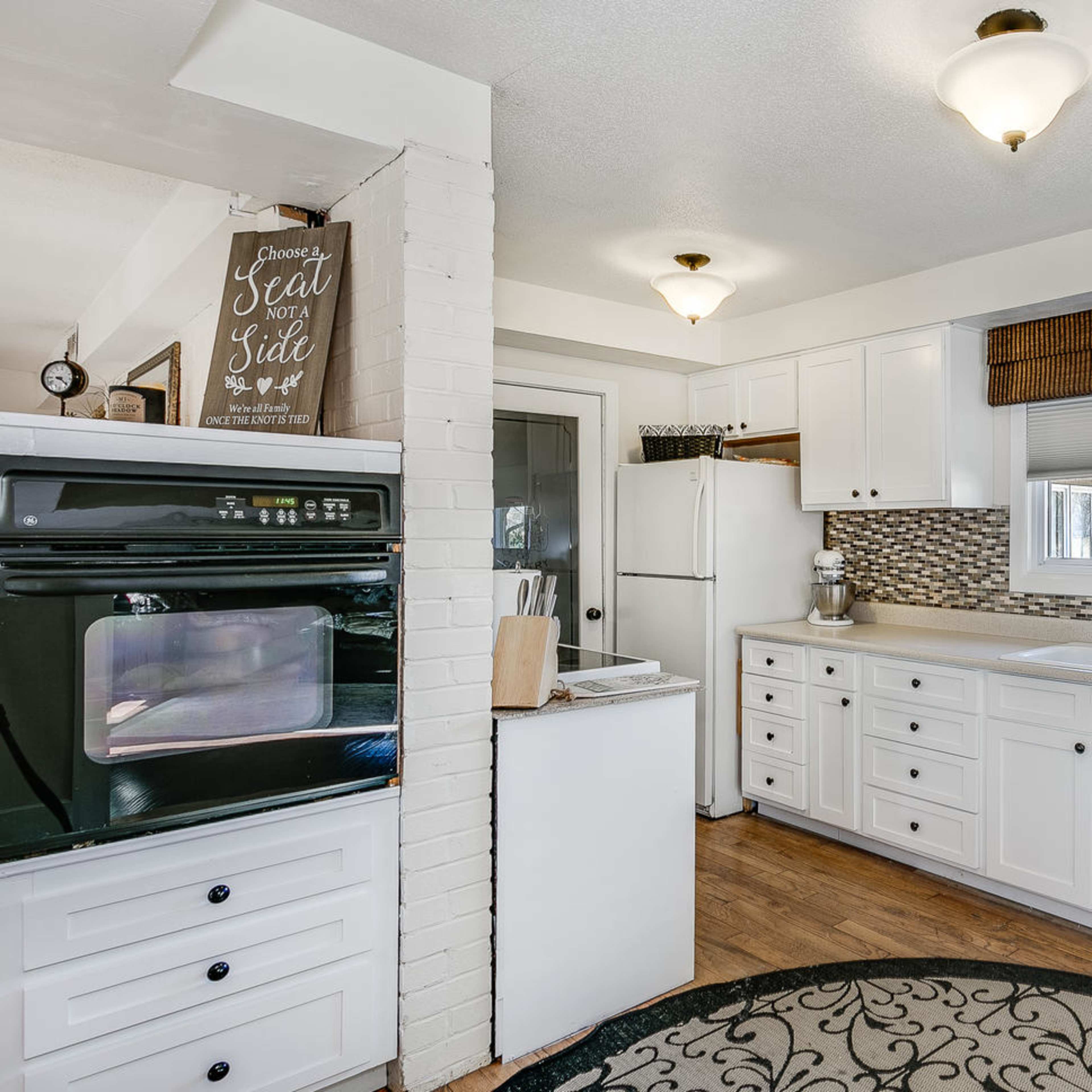 The kitchen features white cabinetry, a dark oven, and a tile backsplash, with a window illuminating the countertop.