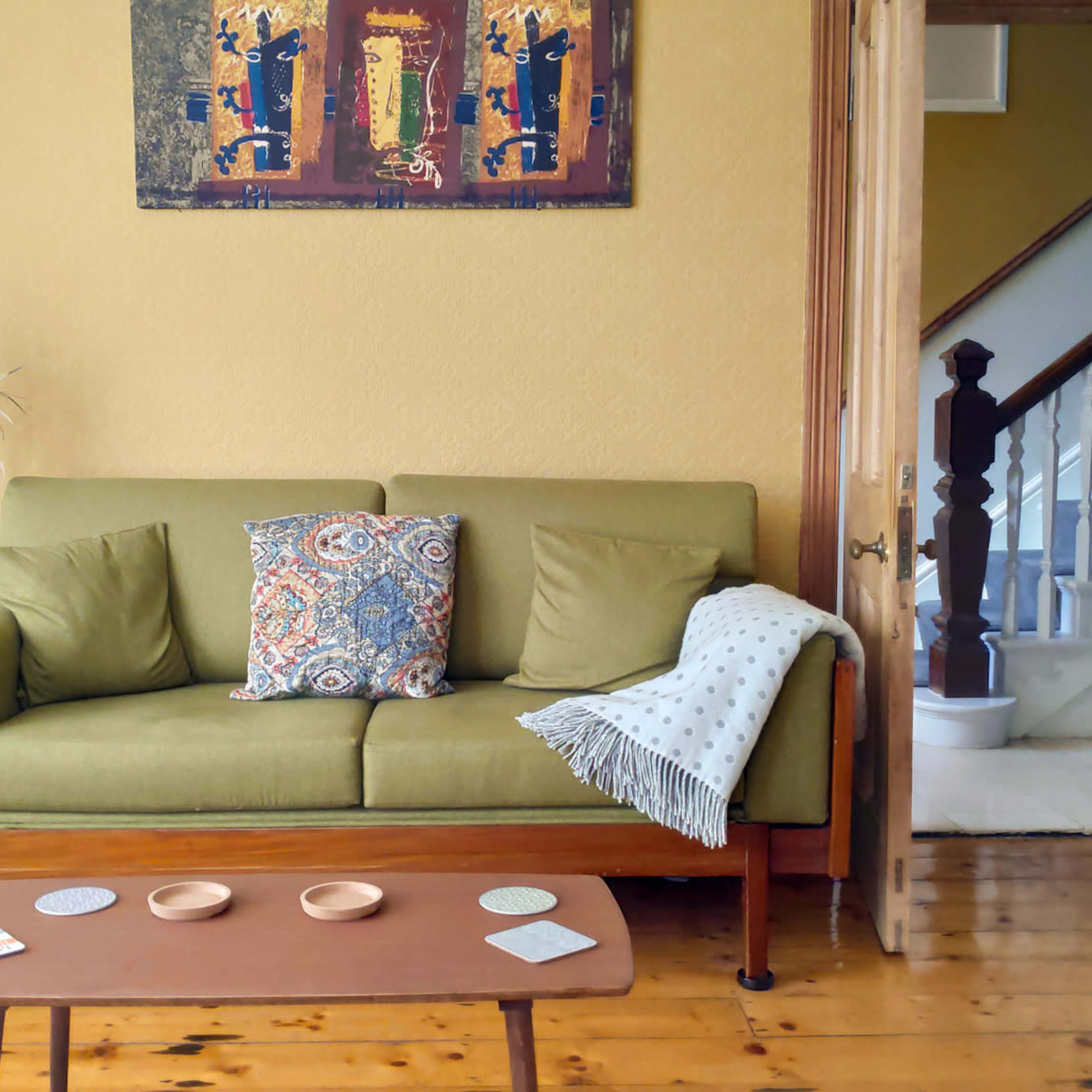 A cozy living room with a green sofa, decorative pillows, a wooden coffee table, and a doorway leading to a staircase.