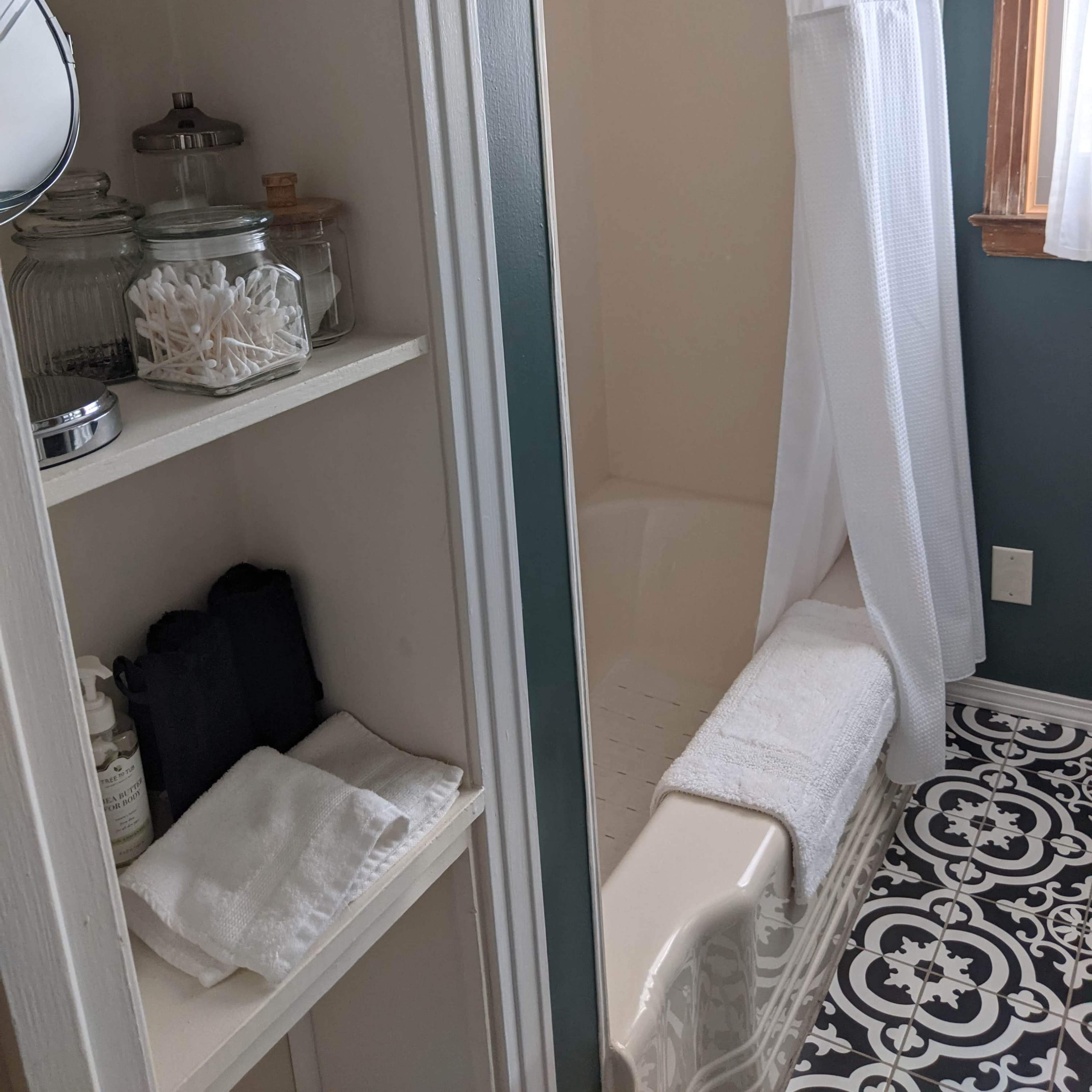 A bathroom with a shower curtain, a clean bathtub, and neatly arranged toiletries on shelves.