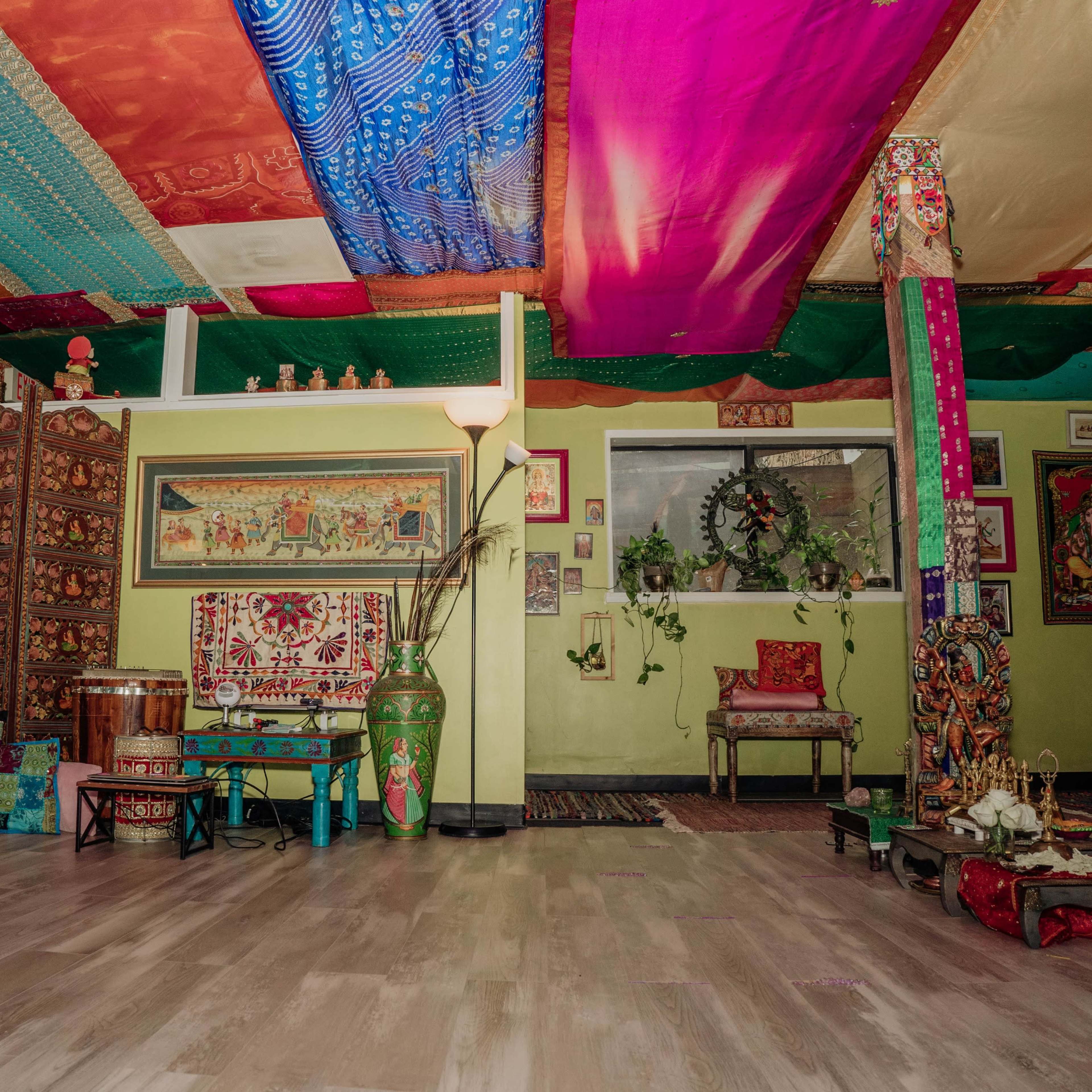 A vibrant and colorful room with a patterned ceiling, adorned walls, and various seating arrangements, including cushions and wooden furniture.
