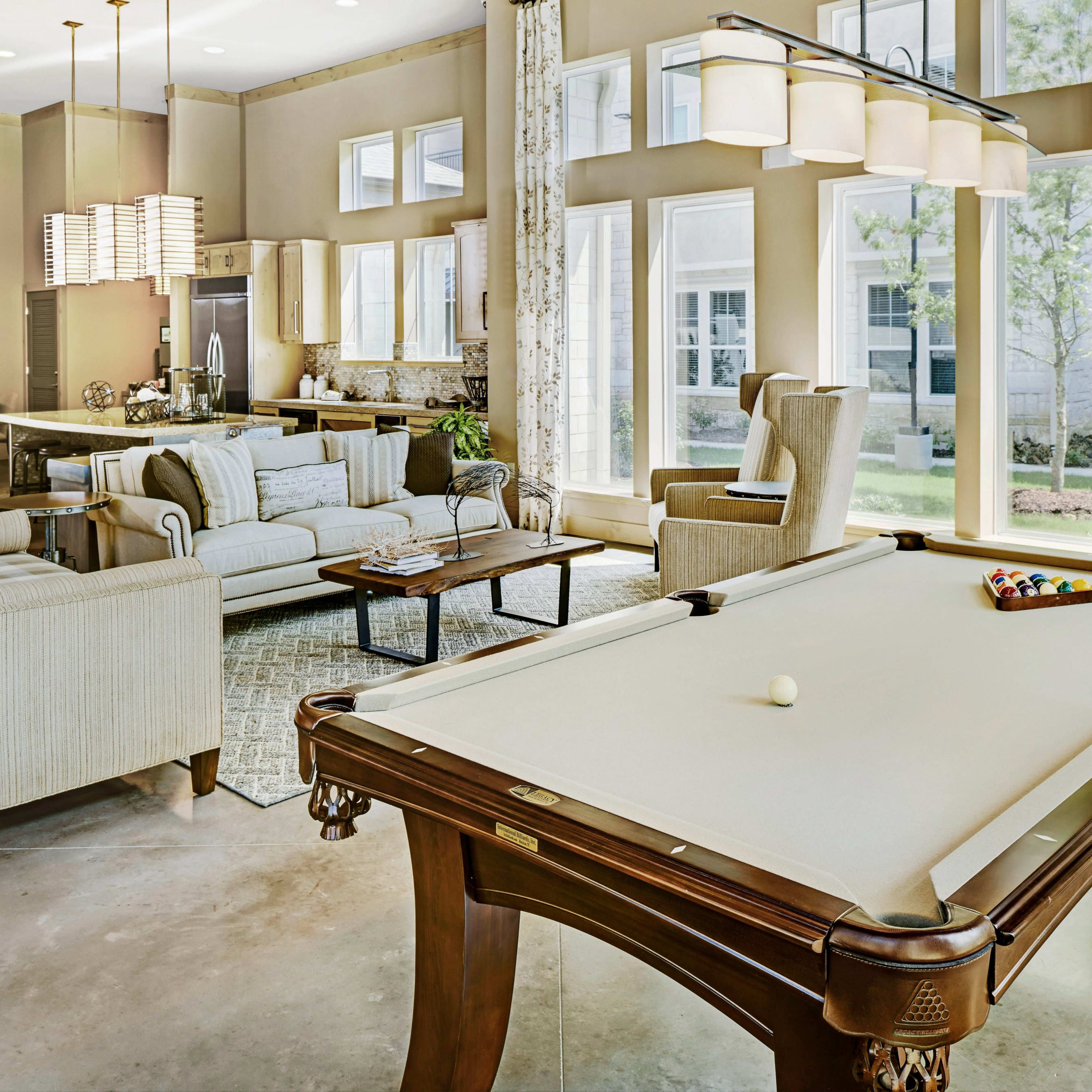 A spacious living area with a pool table, comfortable seating, and large windows overlooking a green outdoor space.