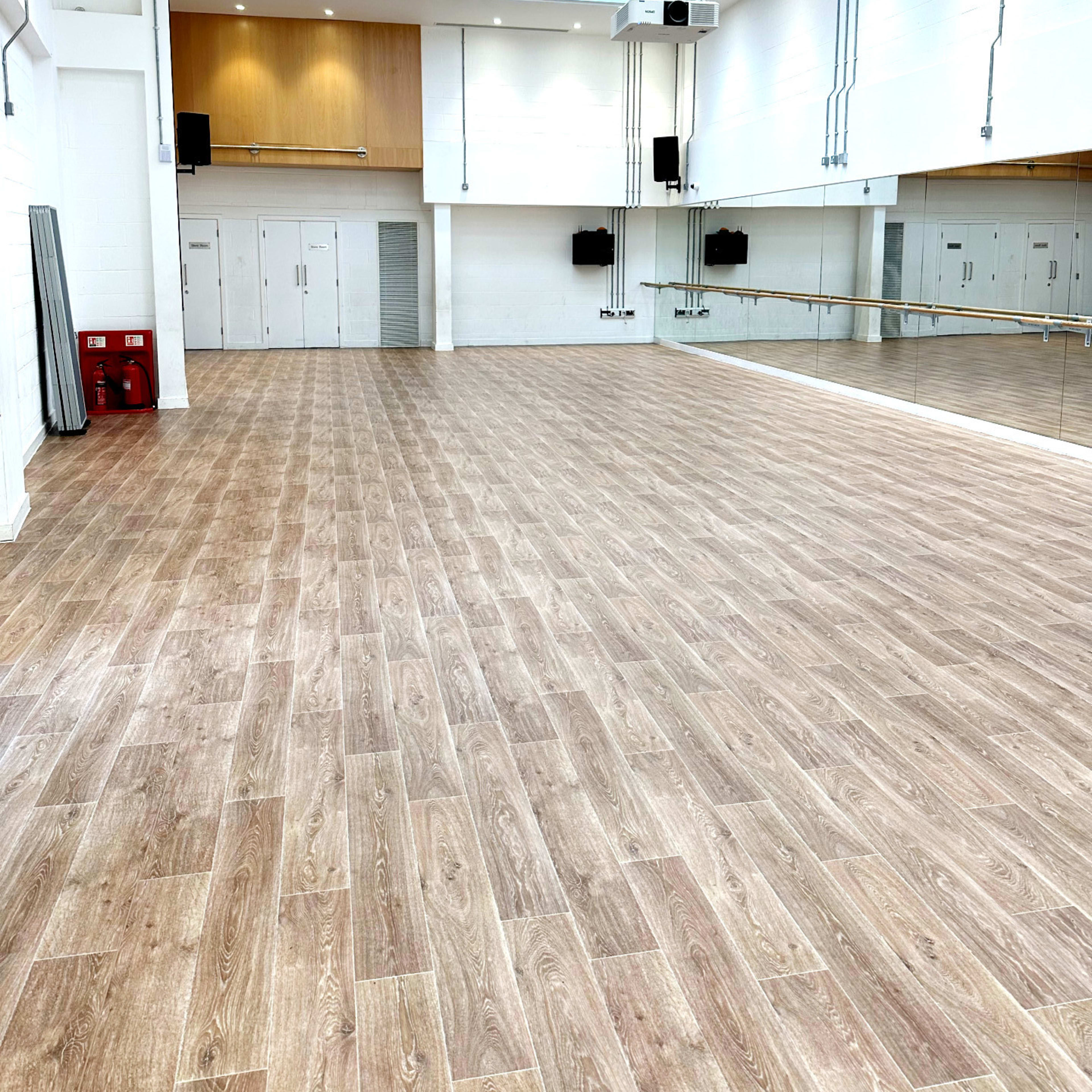 An empty studio space with wooden flooring, large mirrors on one wall, and wall-mounted speakers.