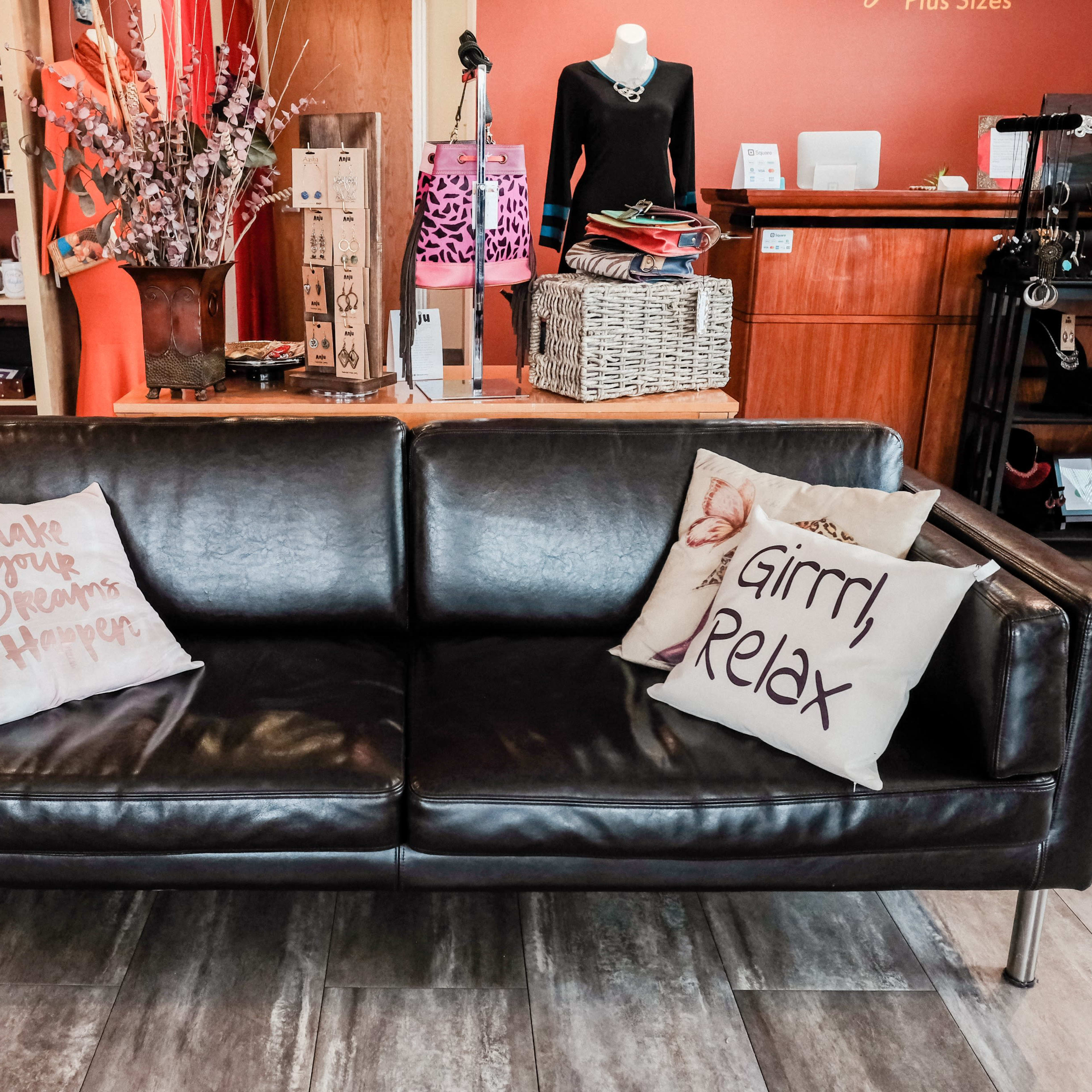 A black leather couch with two decorative pillows in a retail shop that features various products and clothing in the background.
