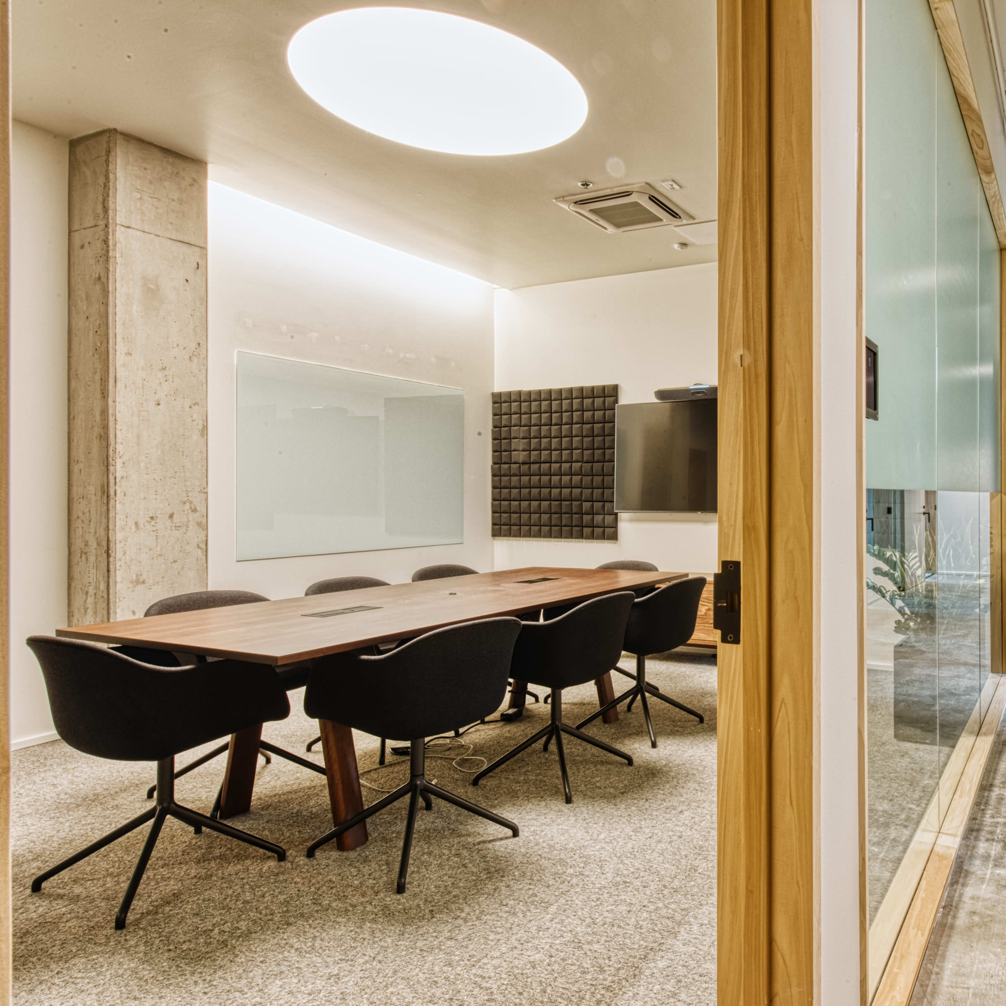 A modern conference room with a wooden table surrounded by black chairs, and a hallway leading to additional office spaces.