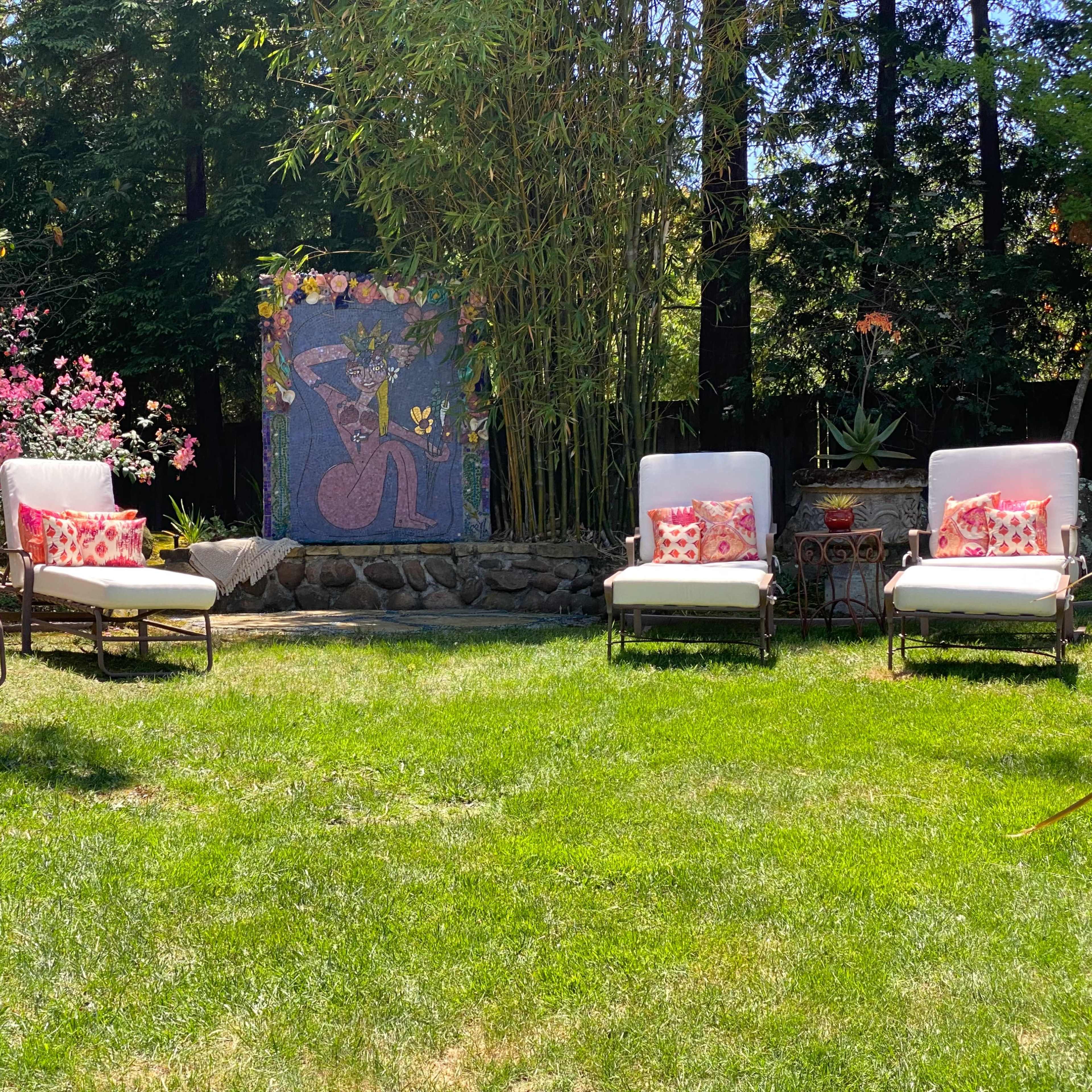 The scene features a grassy backyard with four lounge chairs arranged around a colorful wall mural adorned with plants and flowers.
