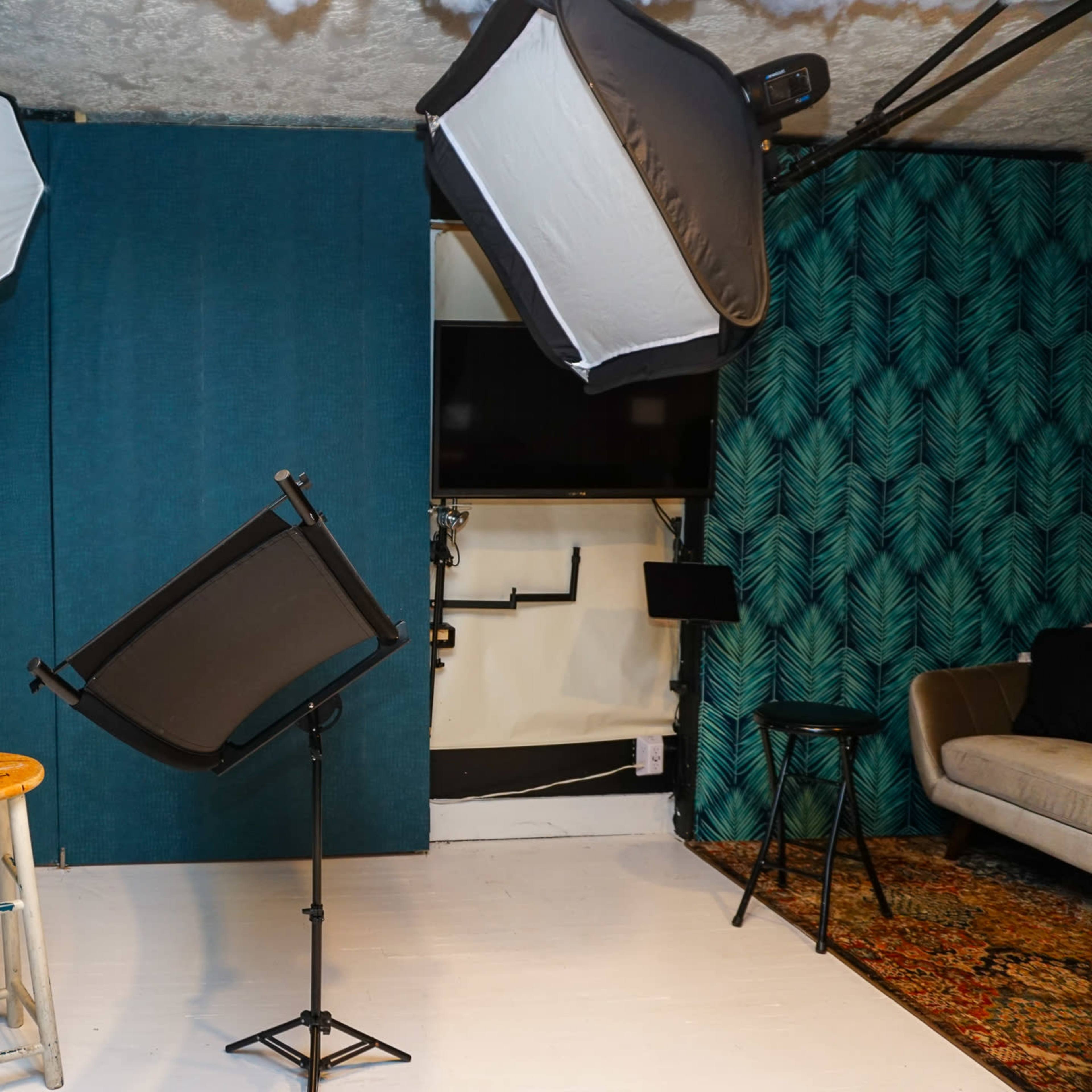 A photography studio with a wooden stool, light modifiers, and a backdrop set against a leaf-patterned wall.