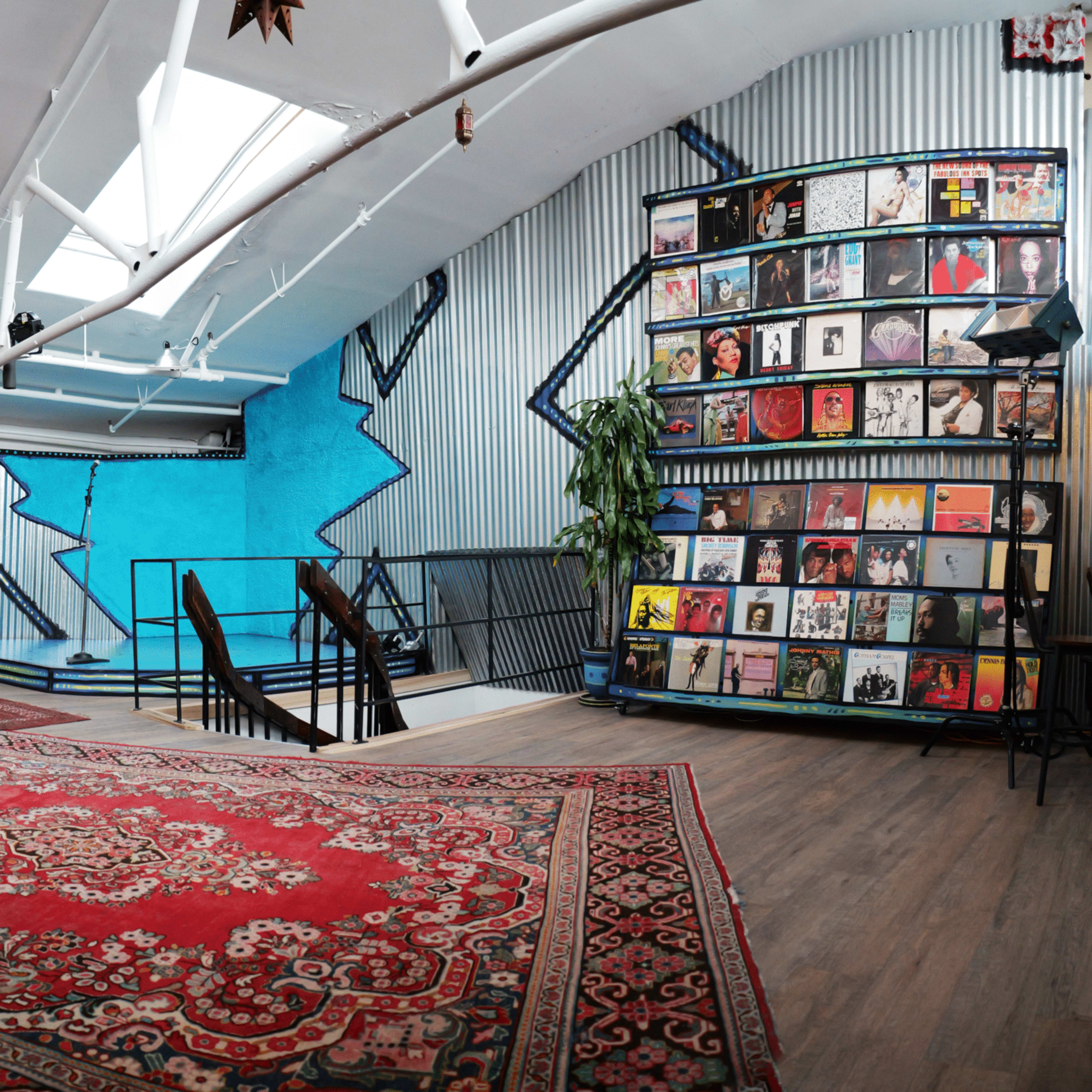 A spacious interior with colorful murals, a patterned rug, and a display of vinyl records on shelves against a blue wall.