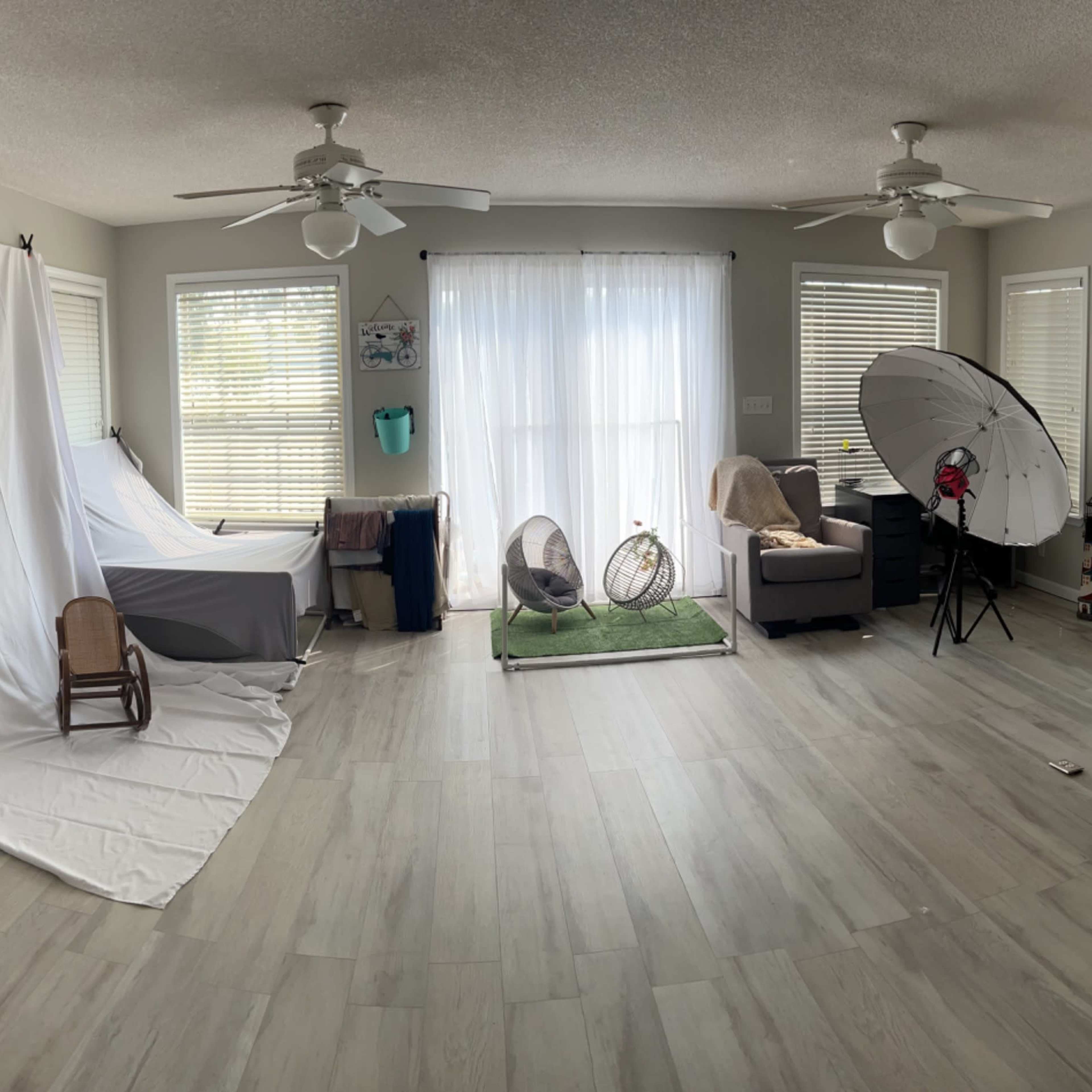 A spacious living room features seating areas, large windows with natural light, and various photography equipment set up in one corner.
