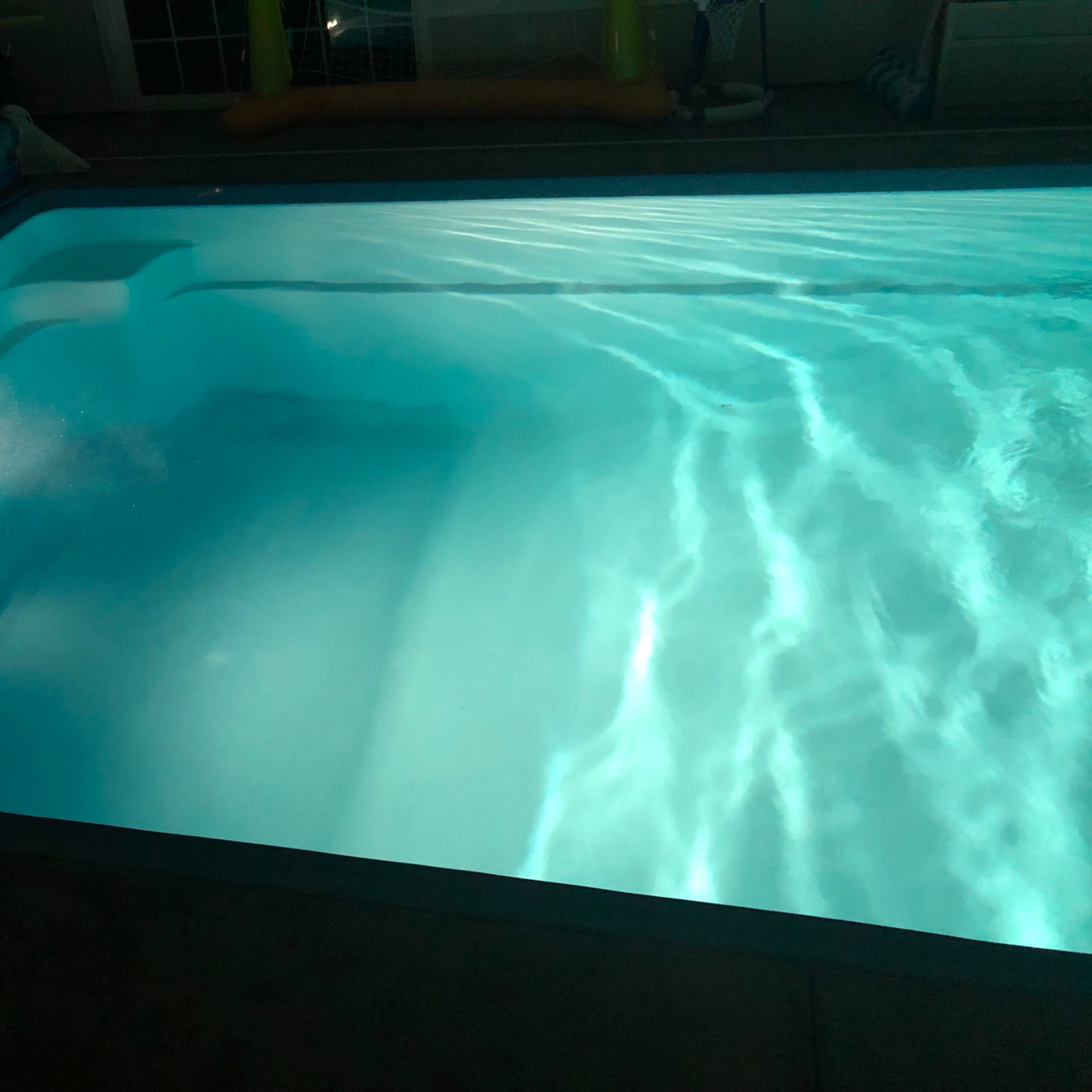 A swimming pool illuminated by underwater lights, reflecting ripples on the surface.