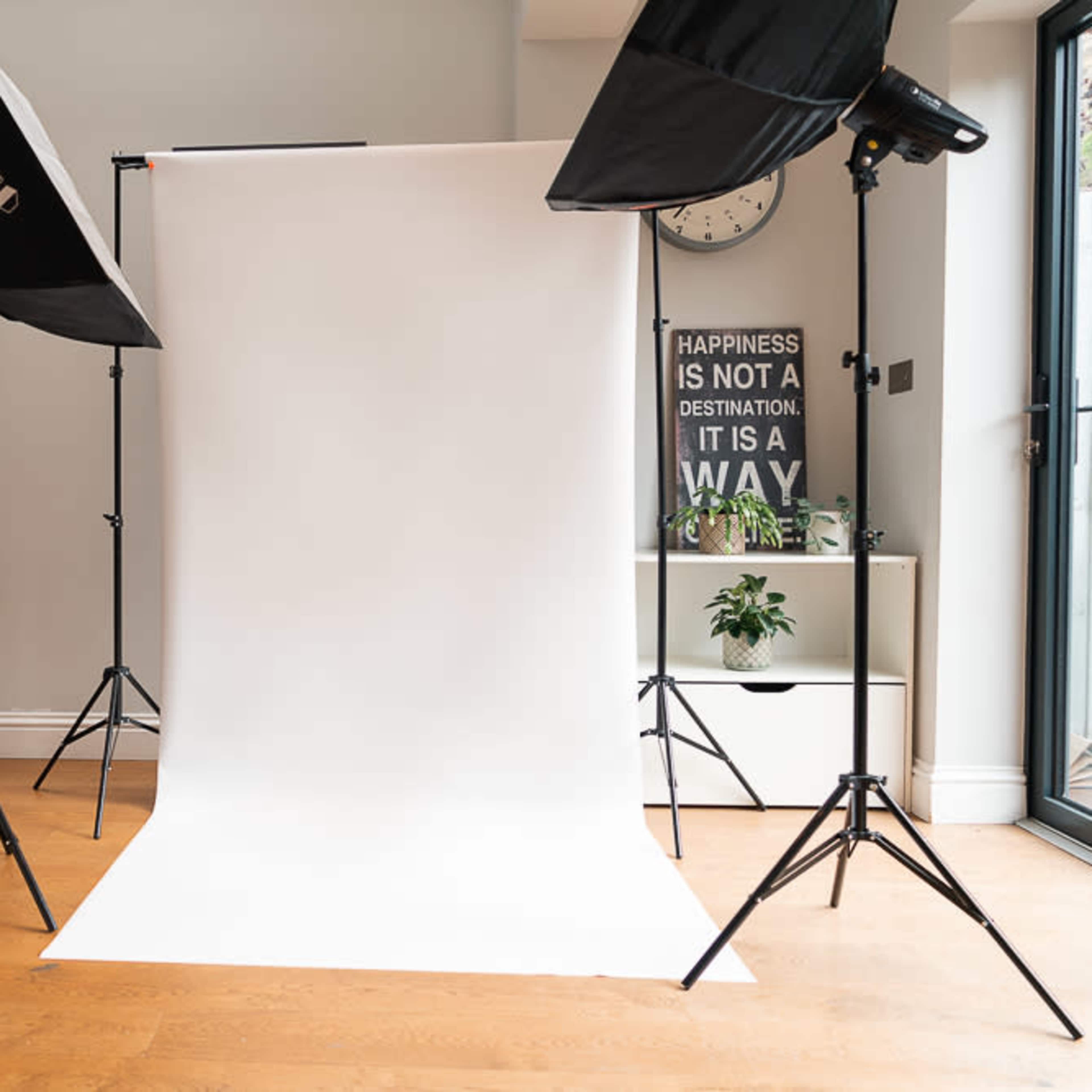 A photography setup features a white backdrop illuminated by two softbox lights in a room with wooden flooring and minimalist decor.