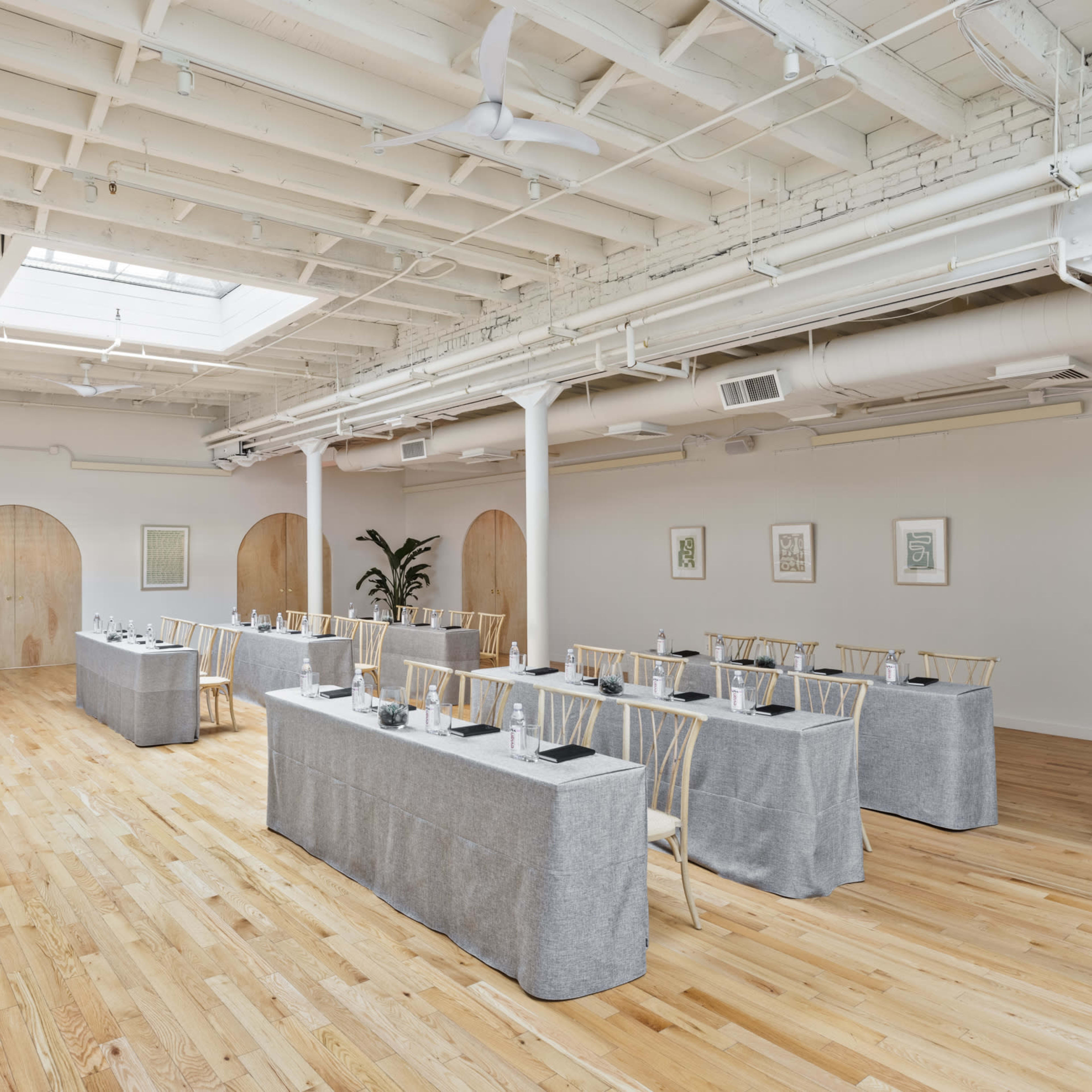 A spacious meeting room with a long table set for a presentation, surrounded by wooden floors and walls adorned with simple decor.