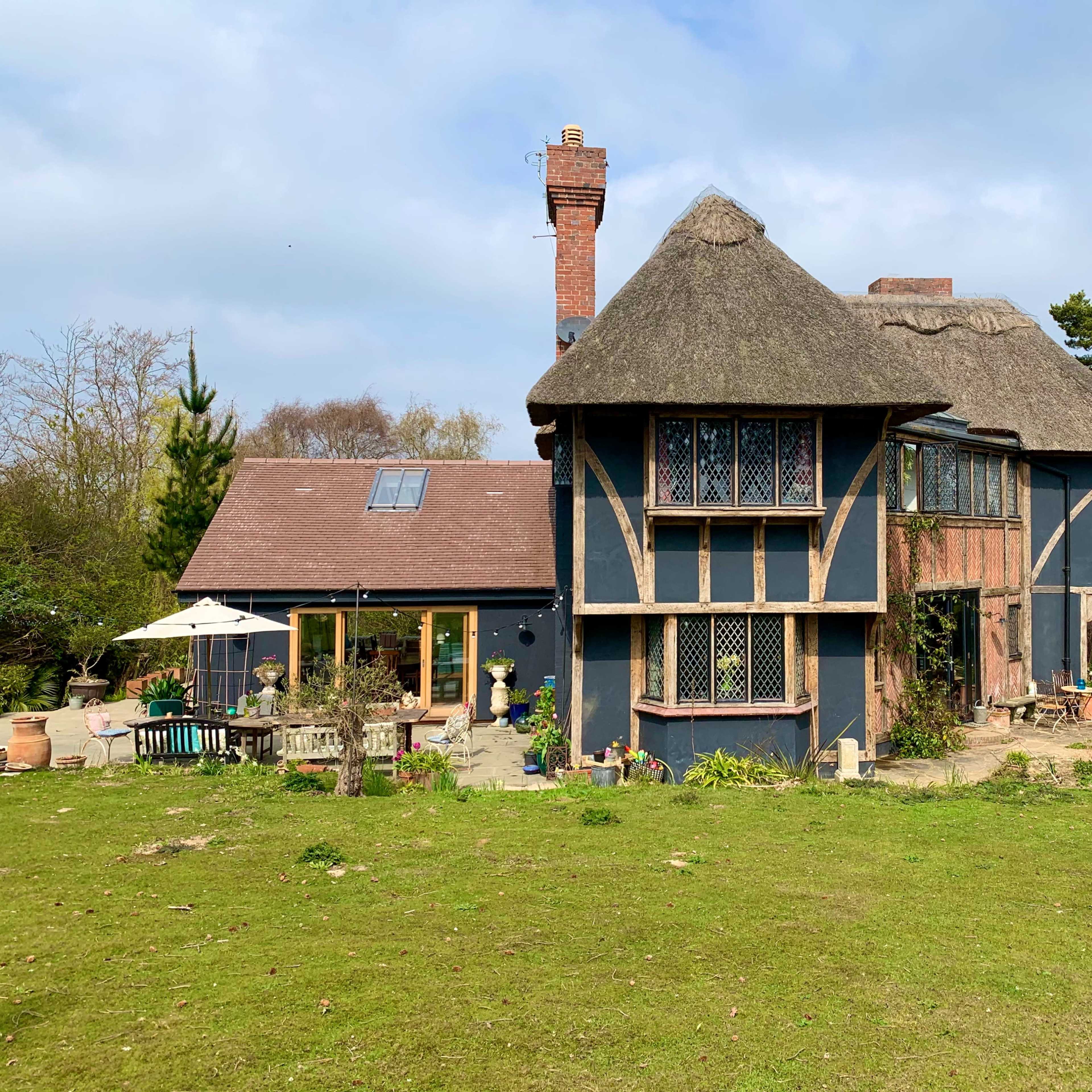 A large, thatched-roof house with a mix of traditional and modern architectural elements, surrounded by greenery.