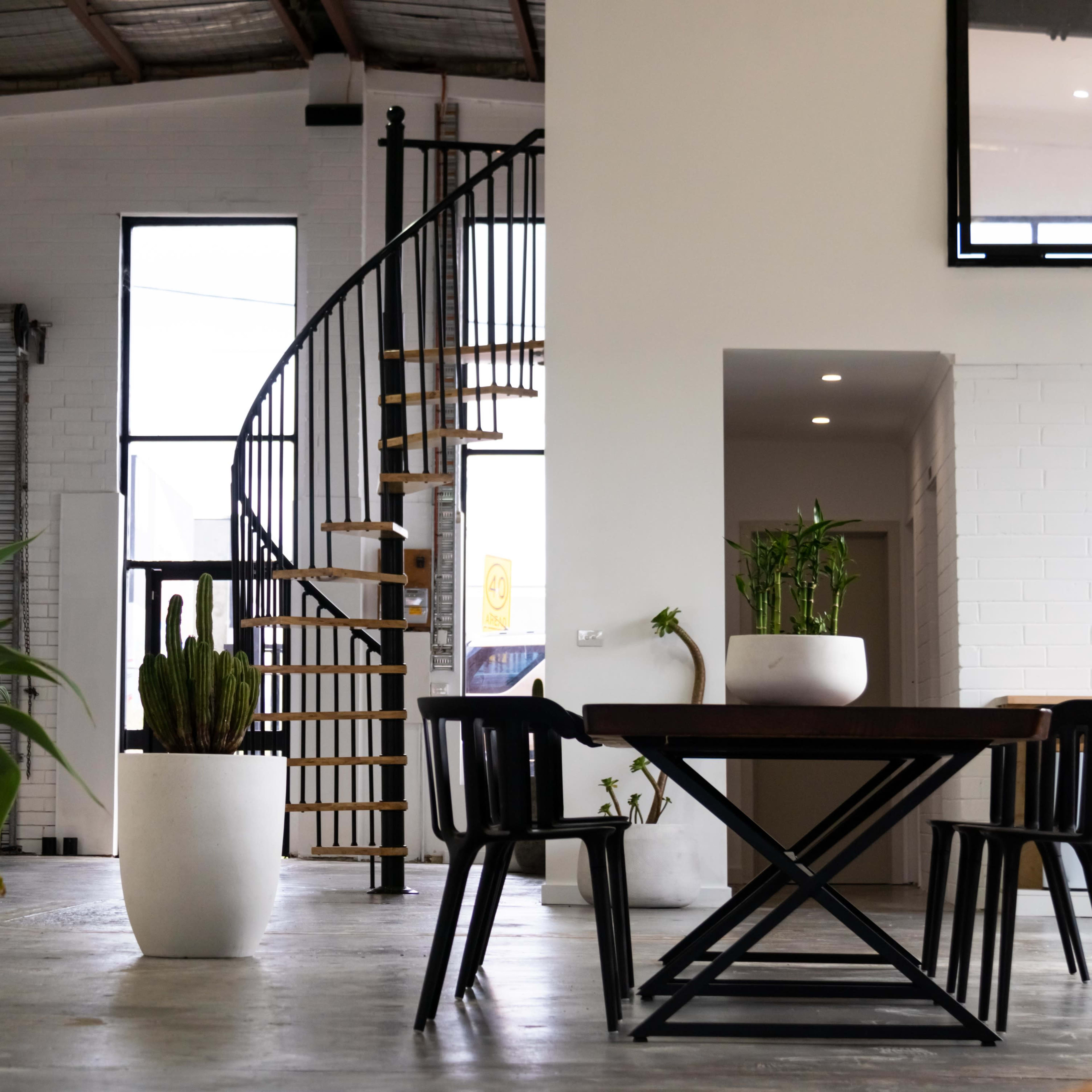 A modern interior space featuring a spiral staircase, a wooden table with black chairs, and several potted plants.