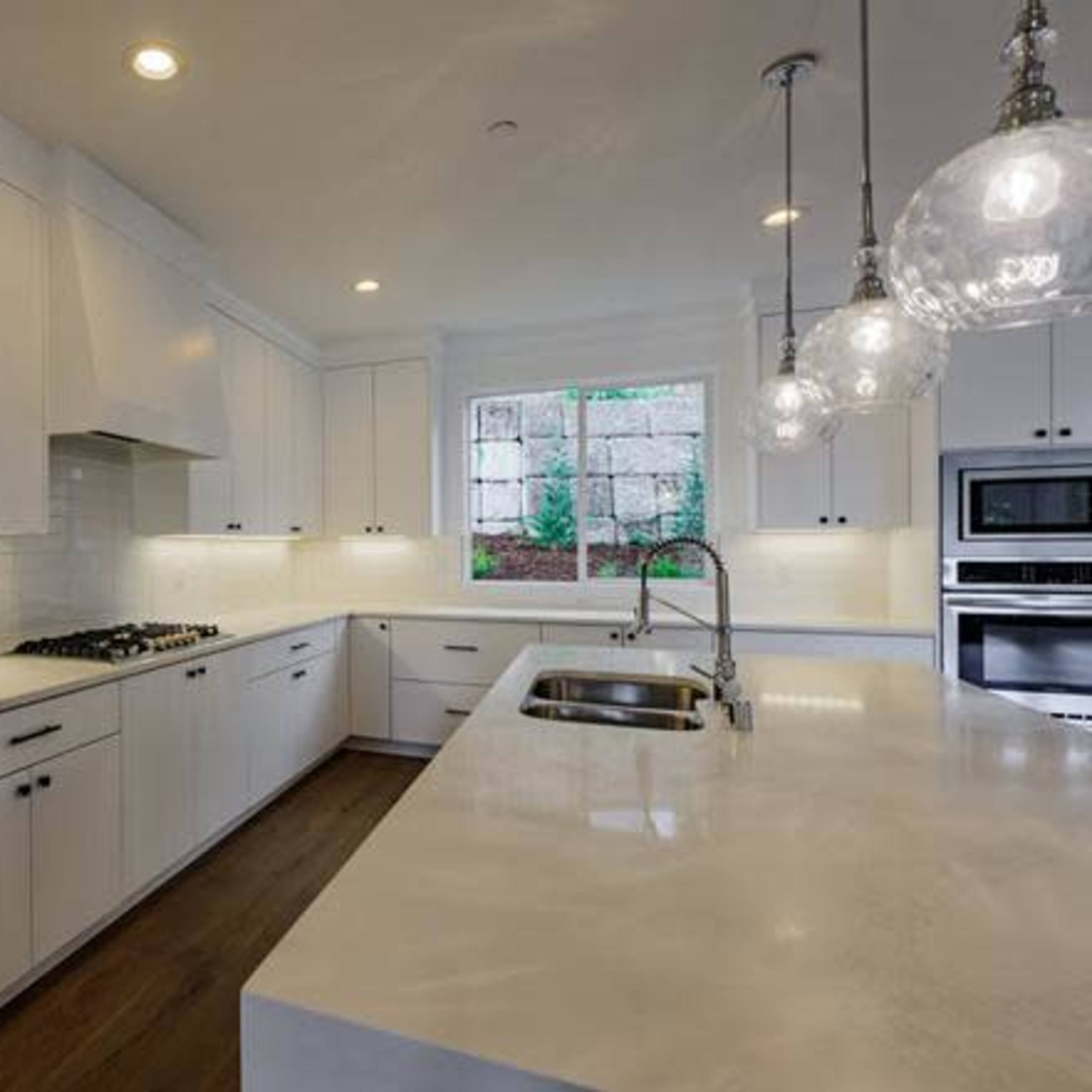 A modern kitchen with white cabinetry, a large island, and pendant lighting above the counter.