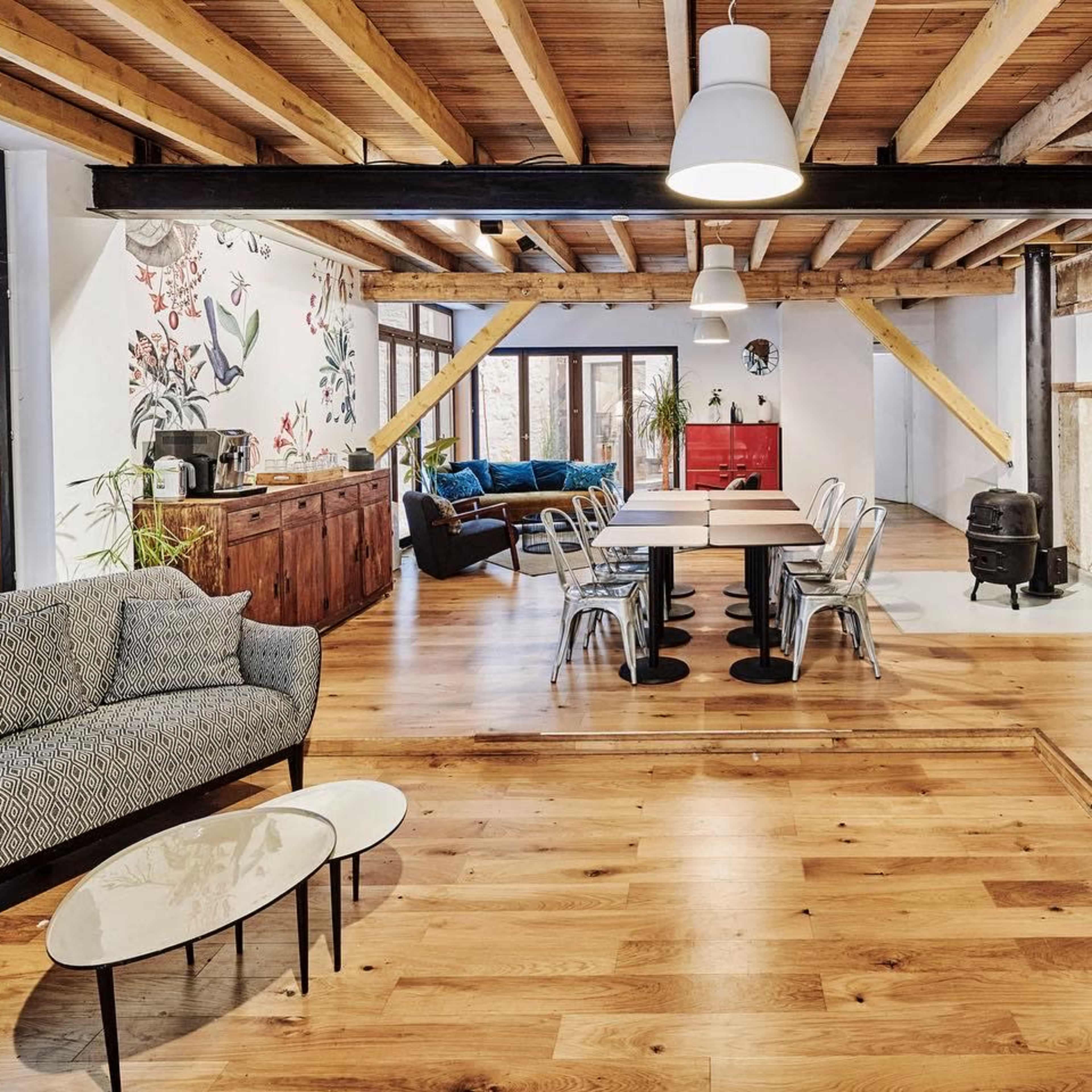 The scene features a spacious living area with wooden beams, a mix of modern and rustic furniture, and a spiral staircase leading to an upper level.