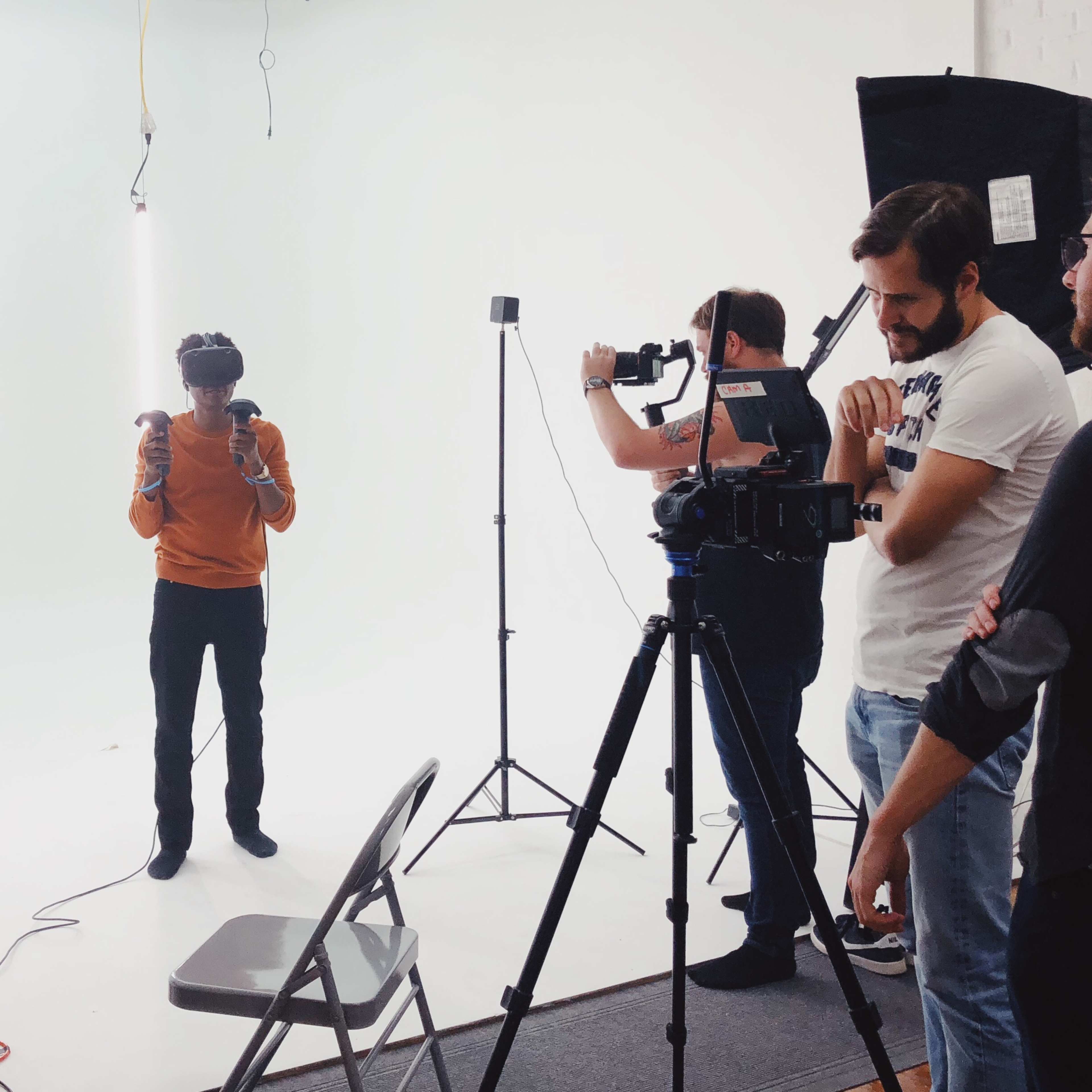 A group of five people sets up camera equipment in a white studio while one person poses for the photo.