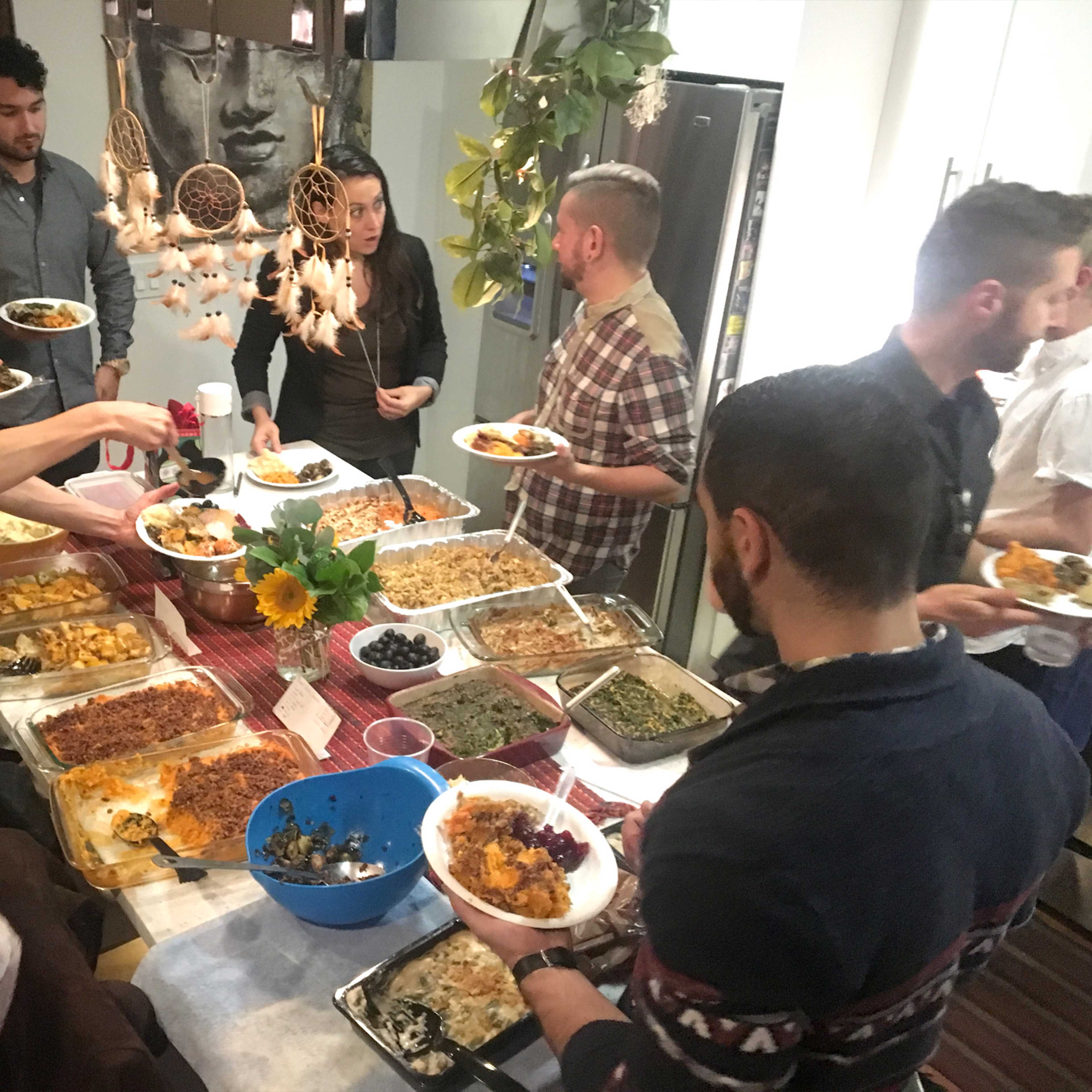 A group of people gathers around a table filled with various dishes, serving food and engaging in conversation.